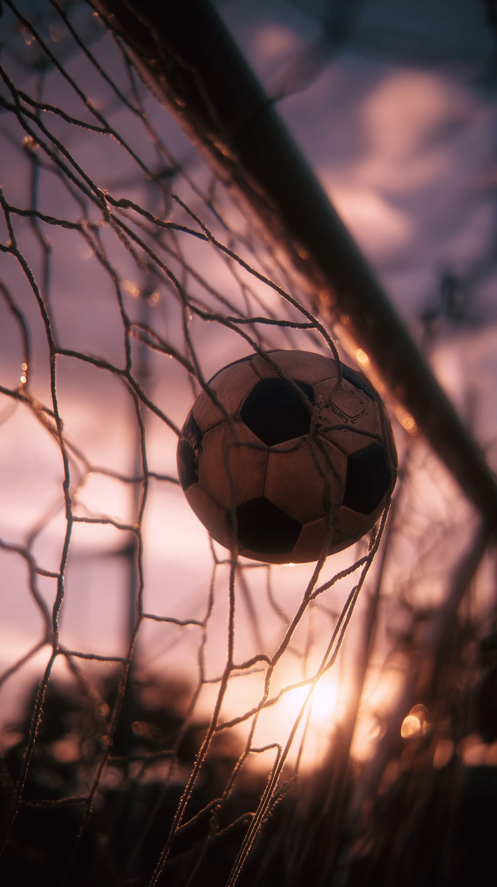 A professional football hitting the net during a scenic sunset with aesthetic lens flares and moody warm tones.