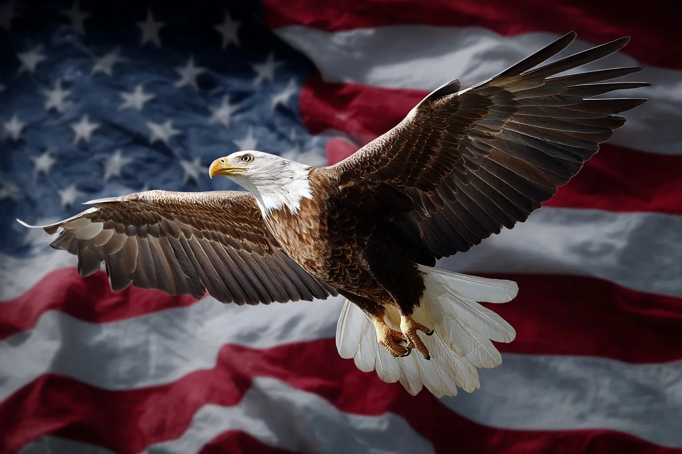 A majestic bald eagle soaring in front of a waving American flag against a clear blue sky.