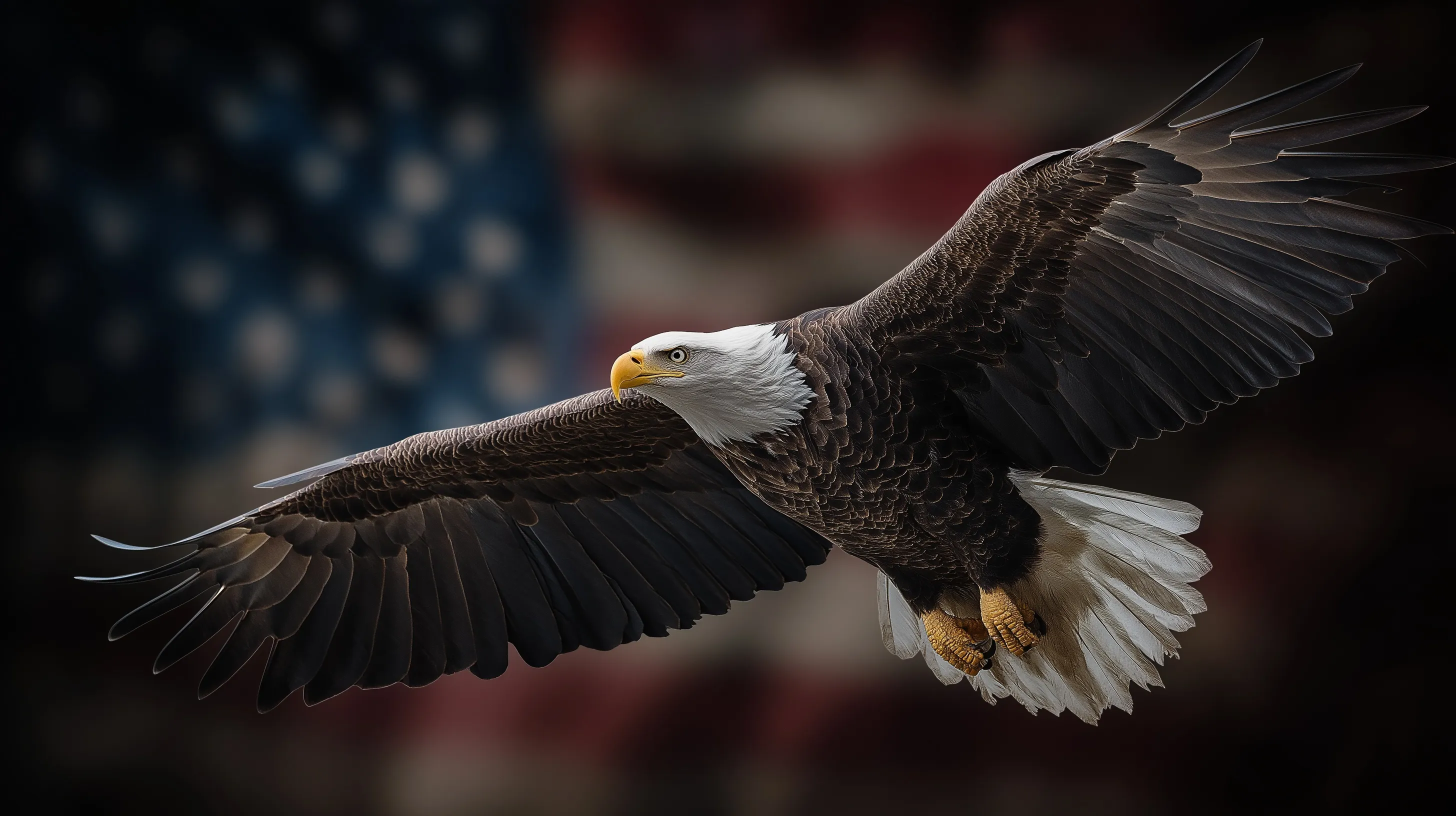 A bald eagle flying head-on while carrying a vibrant American flag in its talons against a clear sky.