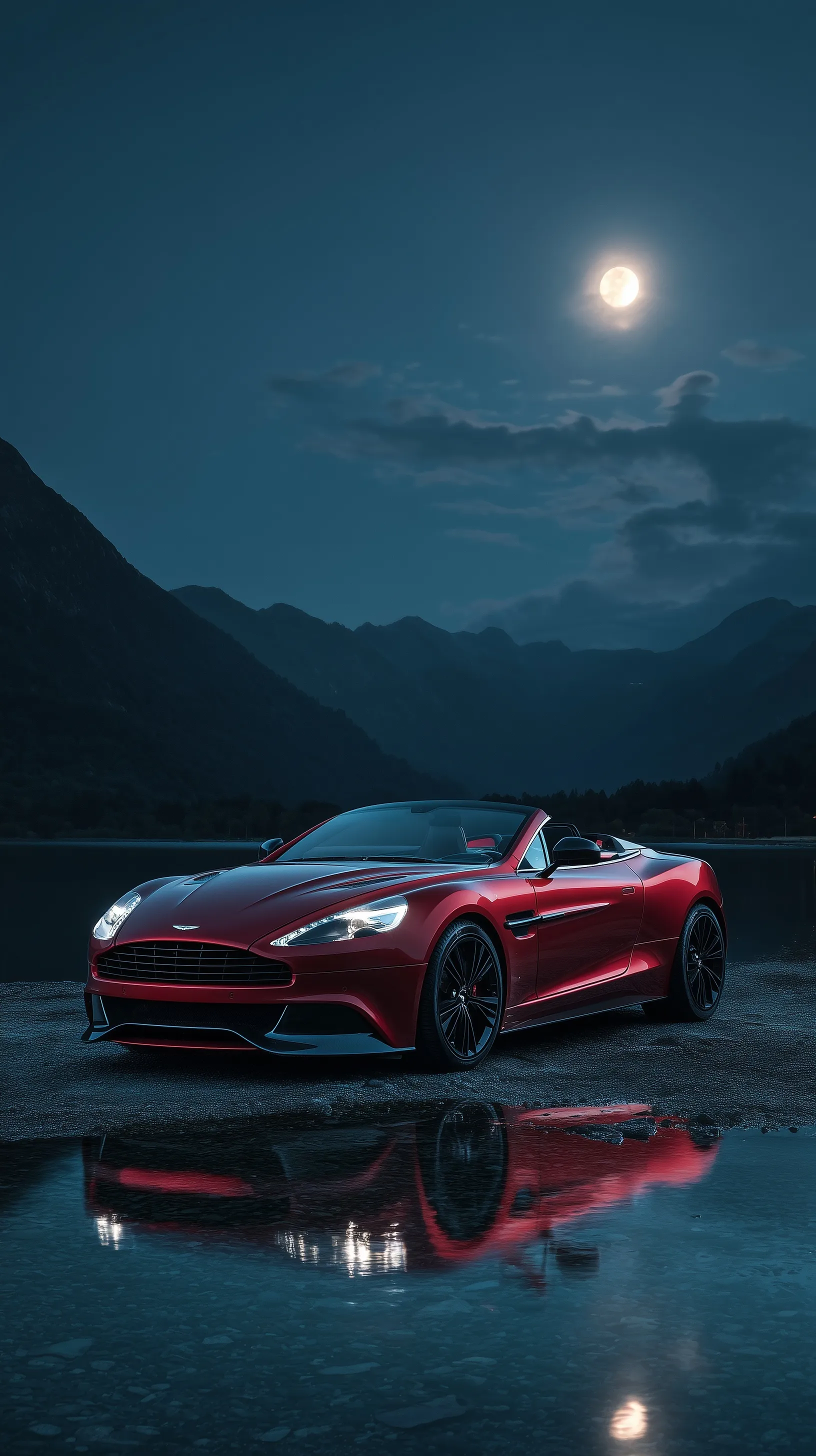 Aston Martin Vanquish Volante parked by a lake at night under a full moon with mountain reflections.