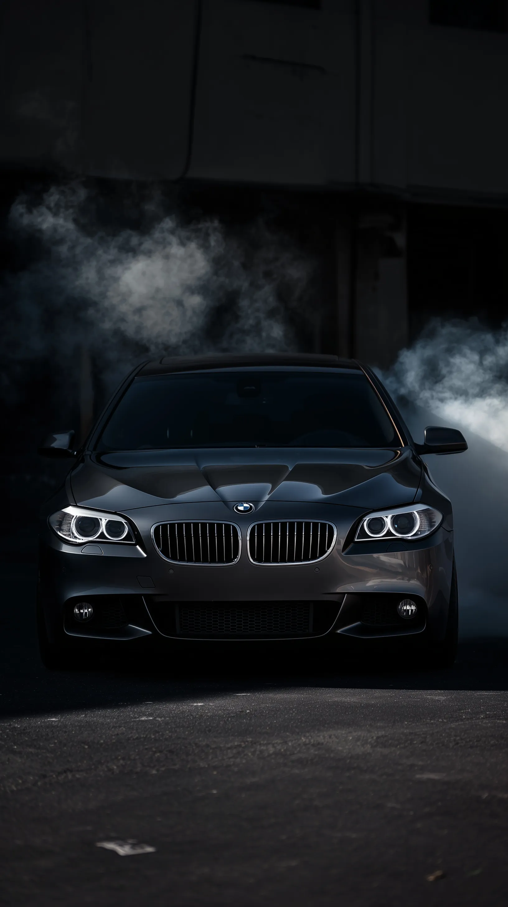 Dark grey BMW 535D F11 with chrome grills and moody smoke in a dramatic front view, perfect for iPhone wallpaper.