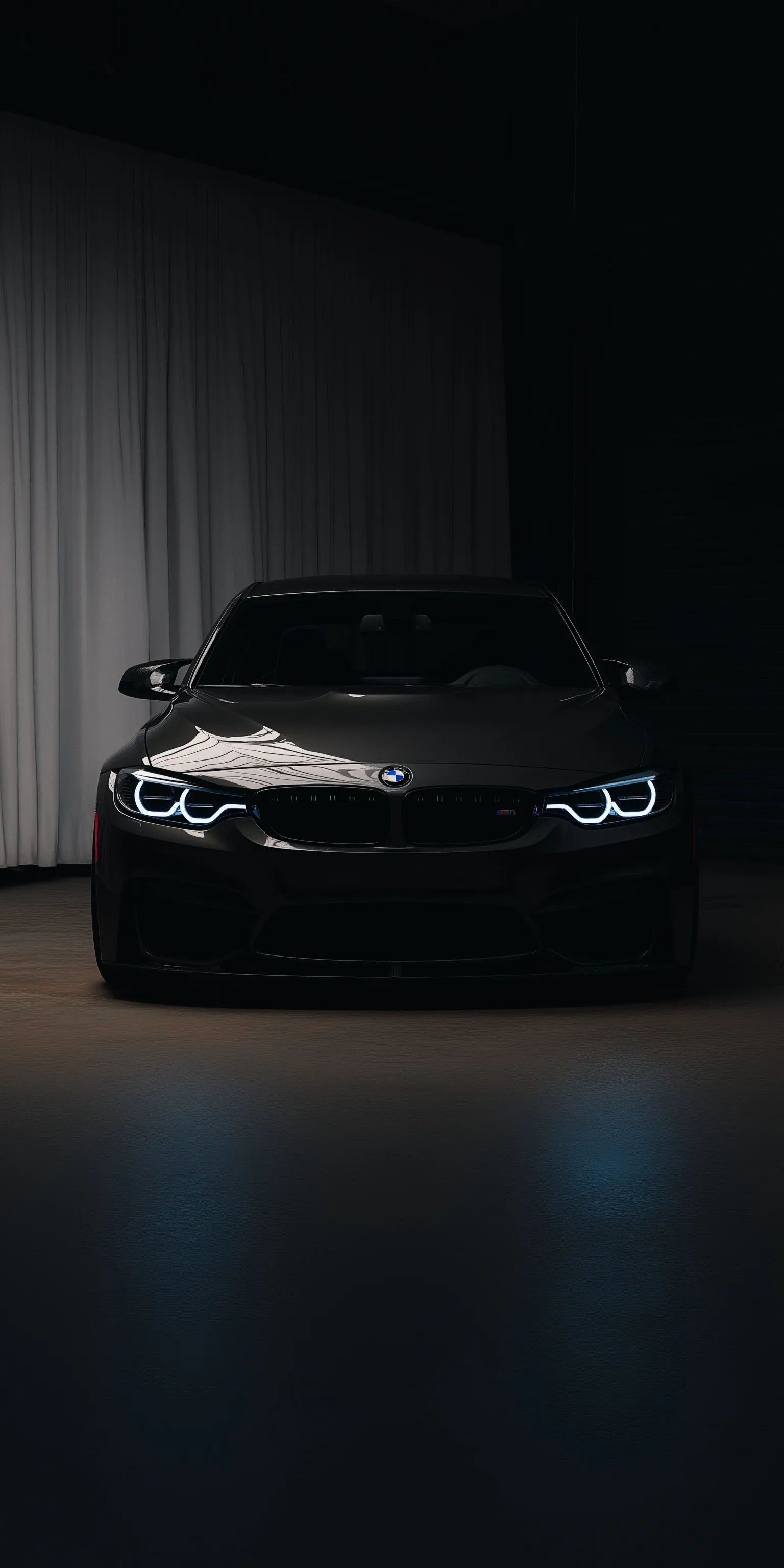 A sleek blacked-out BMW M3 sports car with an aggressive stance in a minimal dark studio setting.