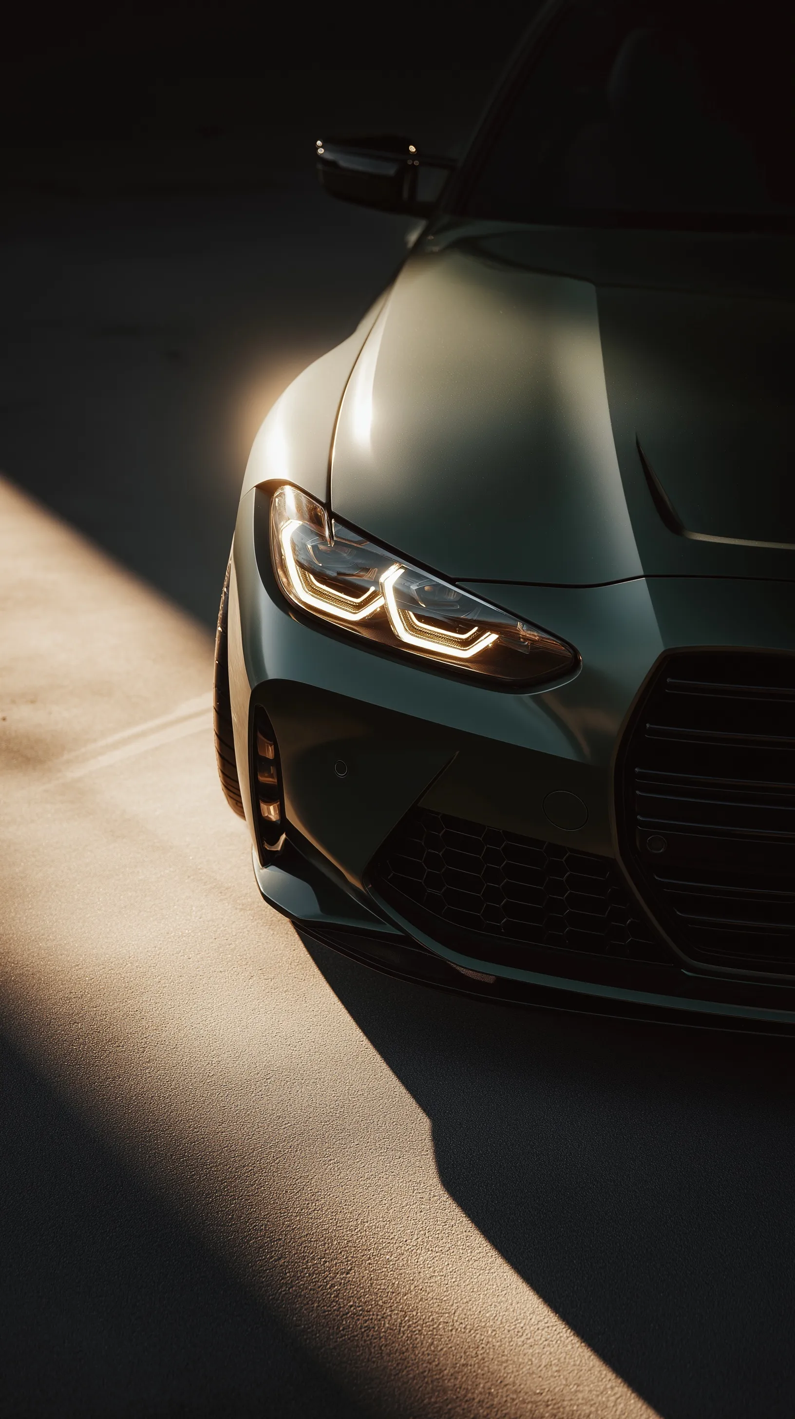 Close-up of a dark green widebody BMW M4 headlamp with reflective hood details for iPhone wallpaper.