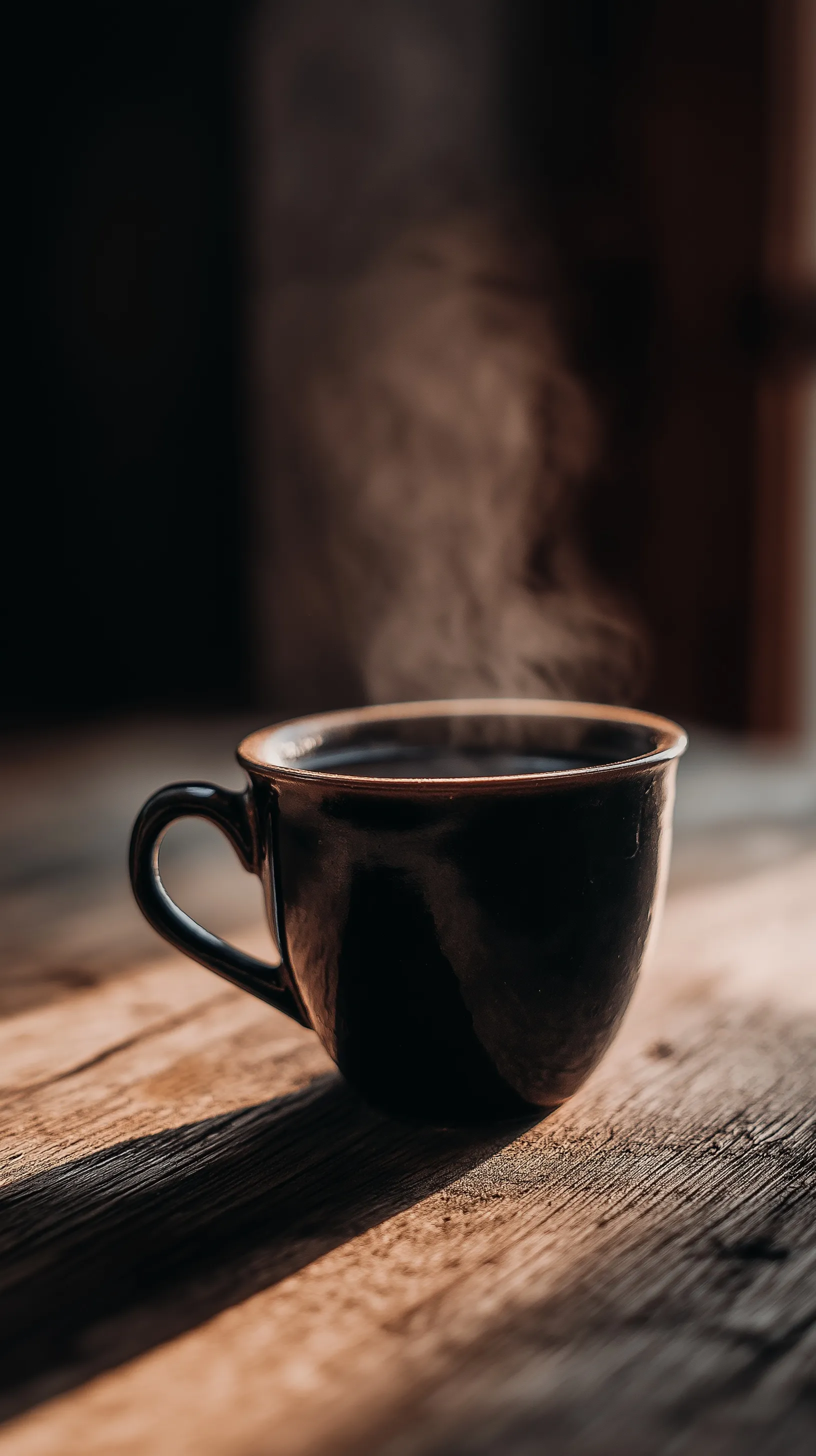 A cinematic black coffee cup on a wooden table with rising steam, moody lighting, and soft bokeh background.