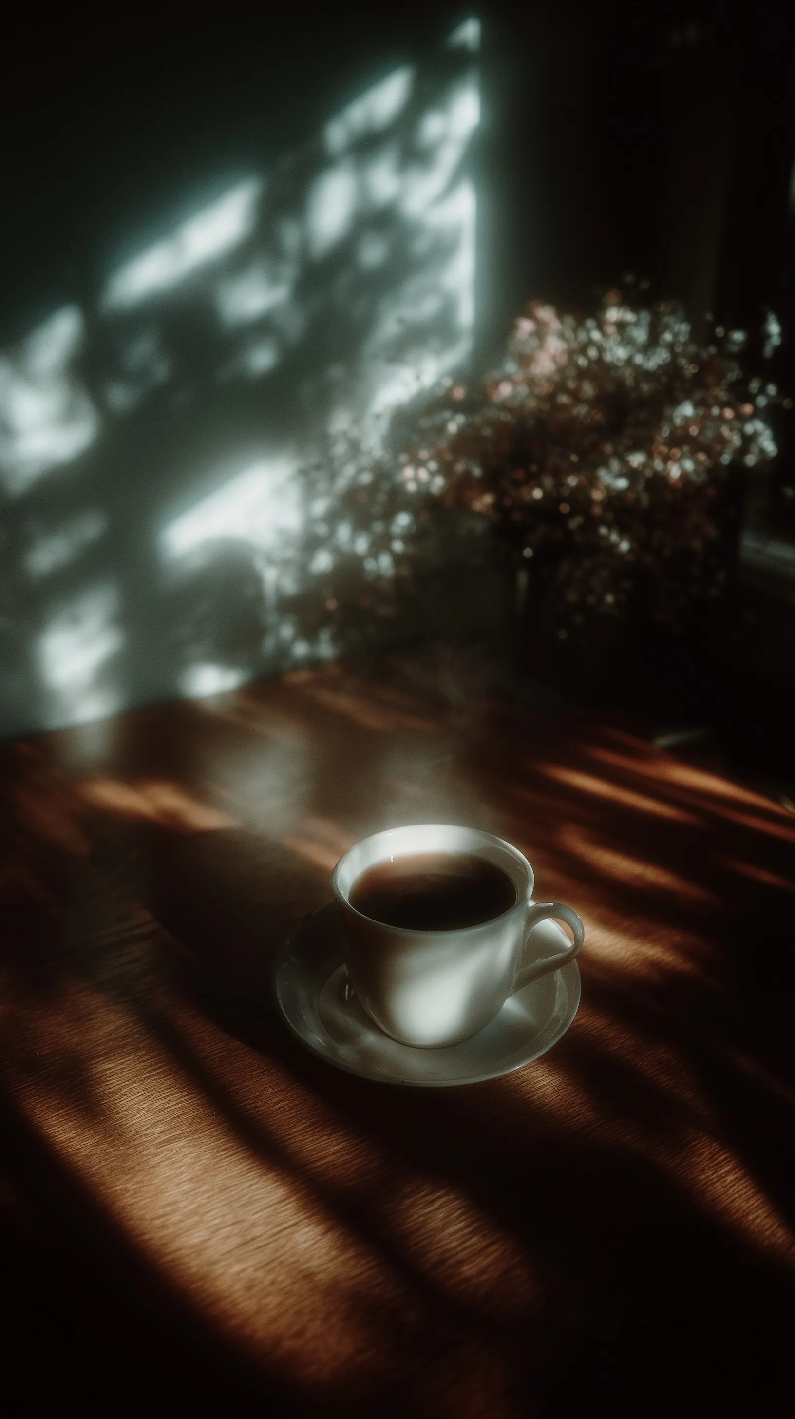 A white cup of black coffee on a rustic wooden table illuminated by soft morning light.