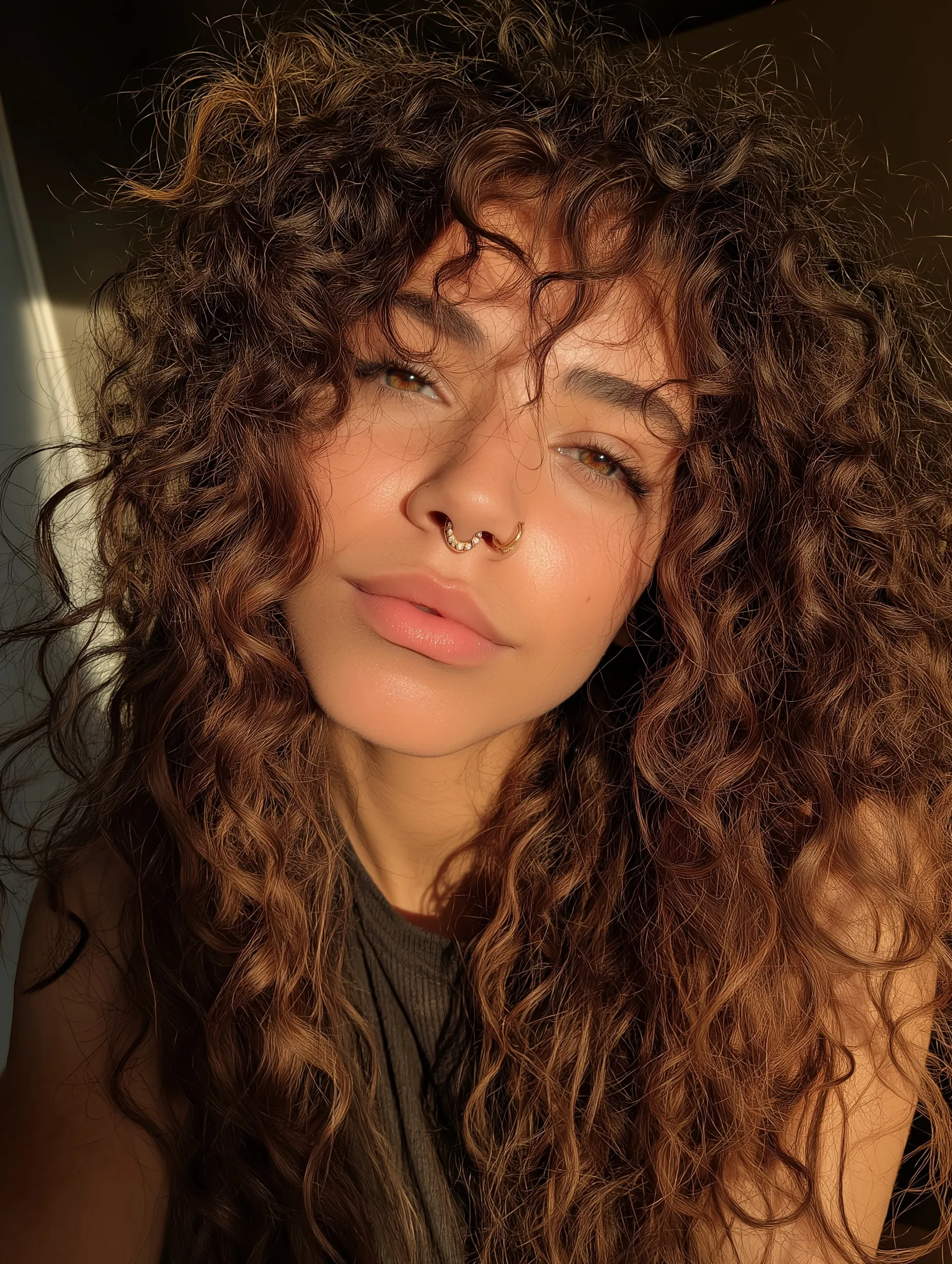 Close-up selfie of a young woman with voluminous 3C curly ombre hair and golden highlights in natural warm light.