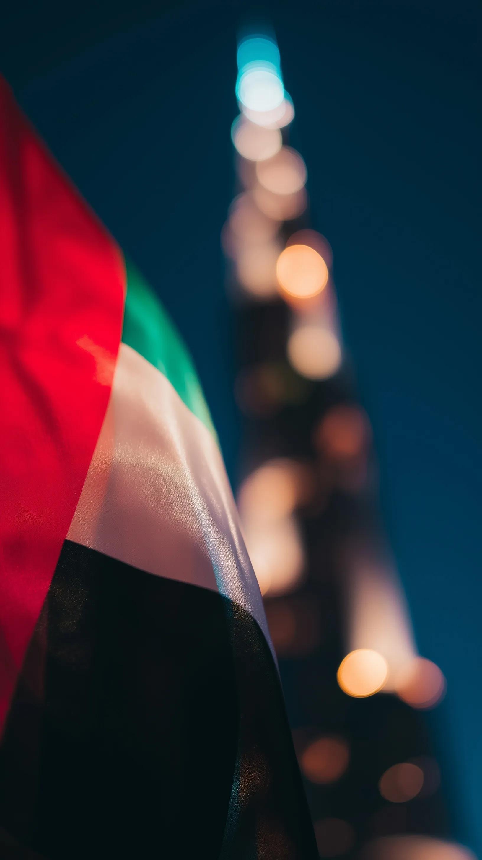 Close-up of UAE flag with blurred Burj Khalifa in background, cinematic Dubai National Day mobile wallpaper.