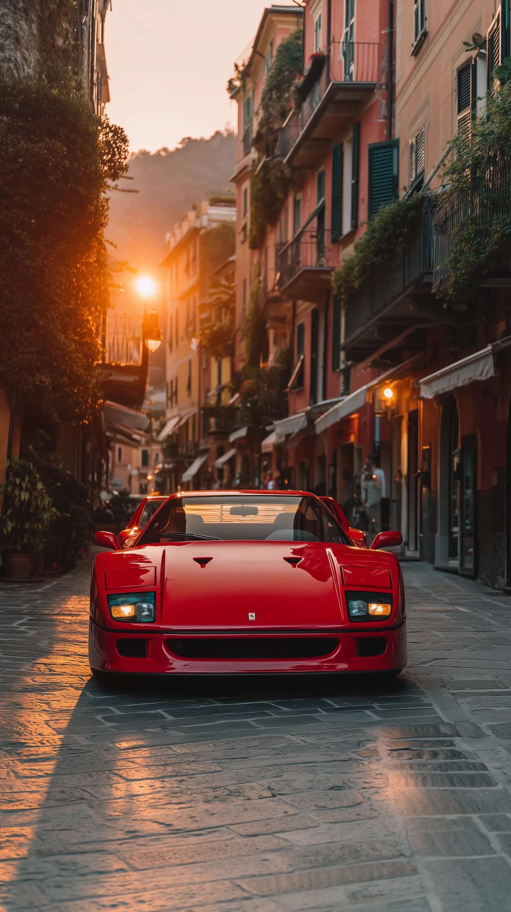 A red Ferrari F40 driving on a cobblestone street in Portofino during a warm golden hour sunset.