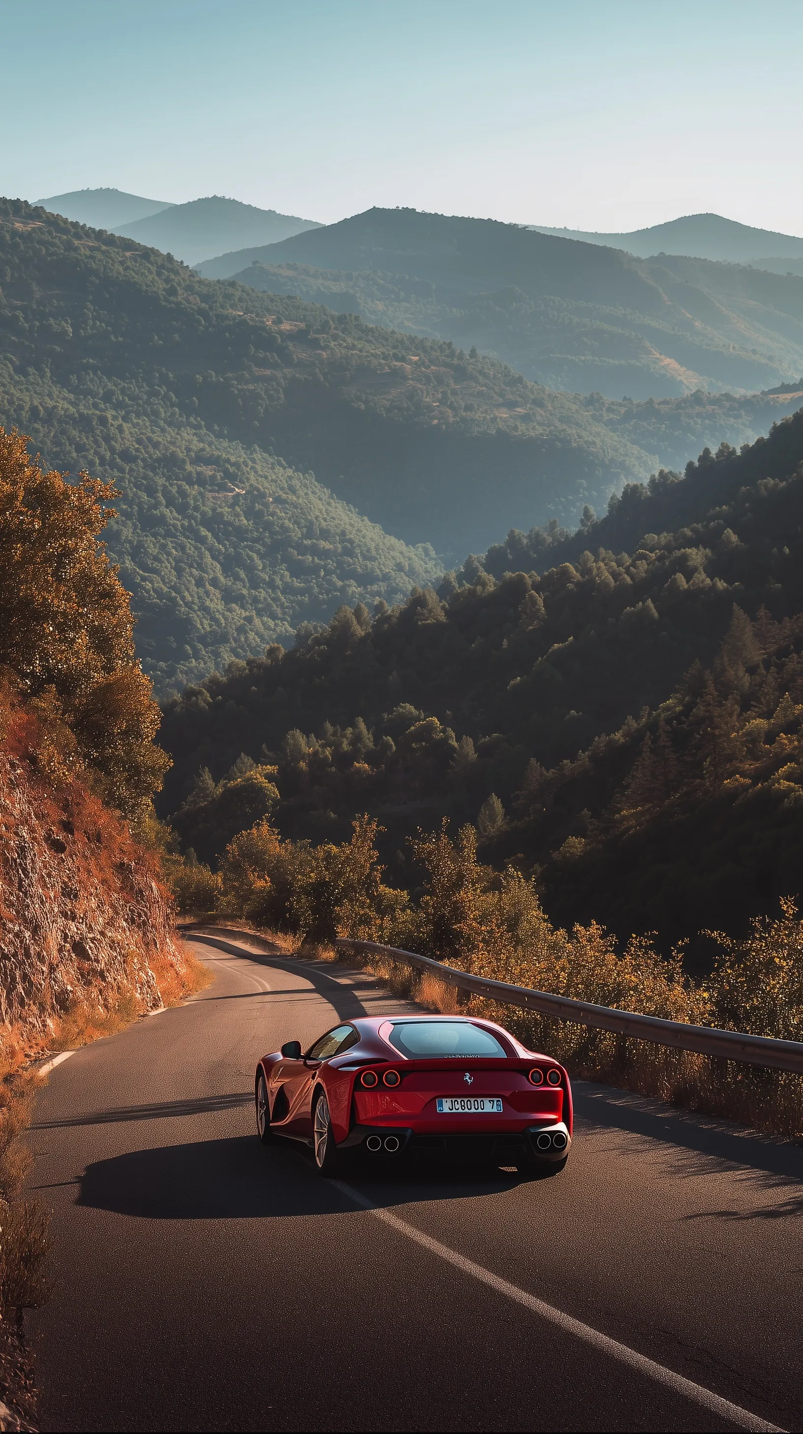 Rear view of a red Ferrari driving along a scenic mountain road, perfect for an iPhone wallpaper.