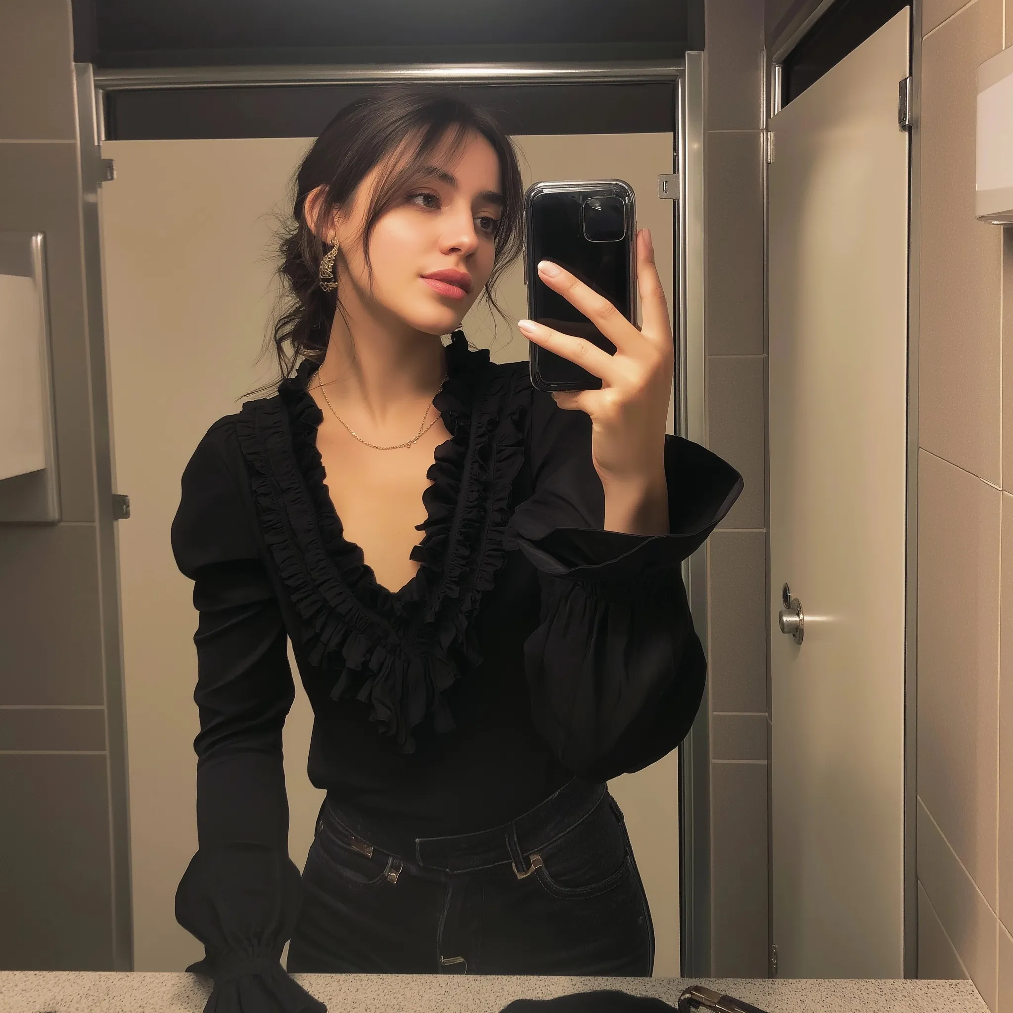 A 23-year-old woman taking a mirror selfie in a black ruffled blouse and jeans, perfect for a first date outfit.