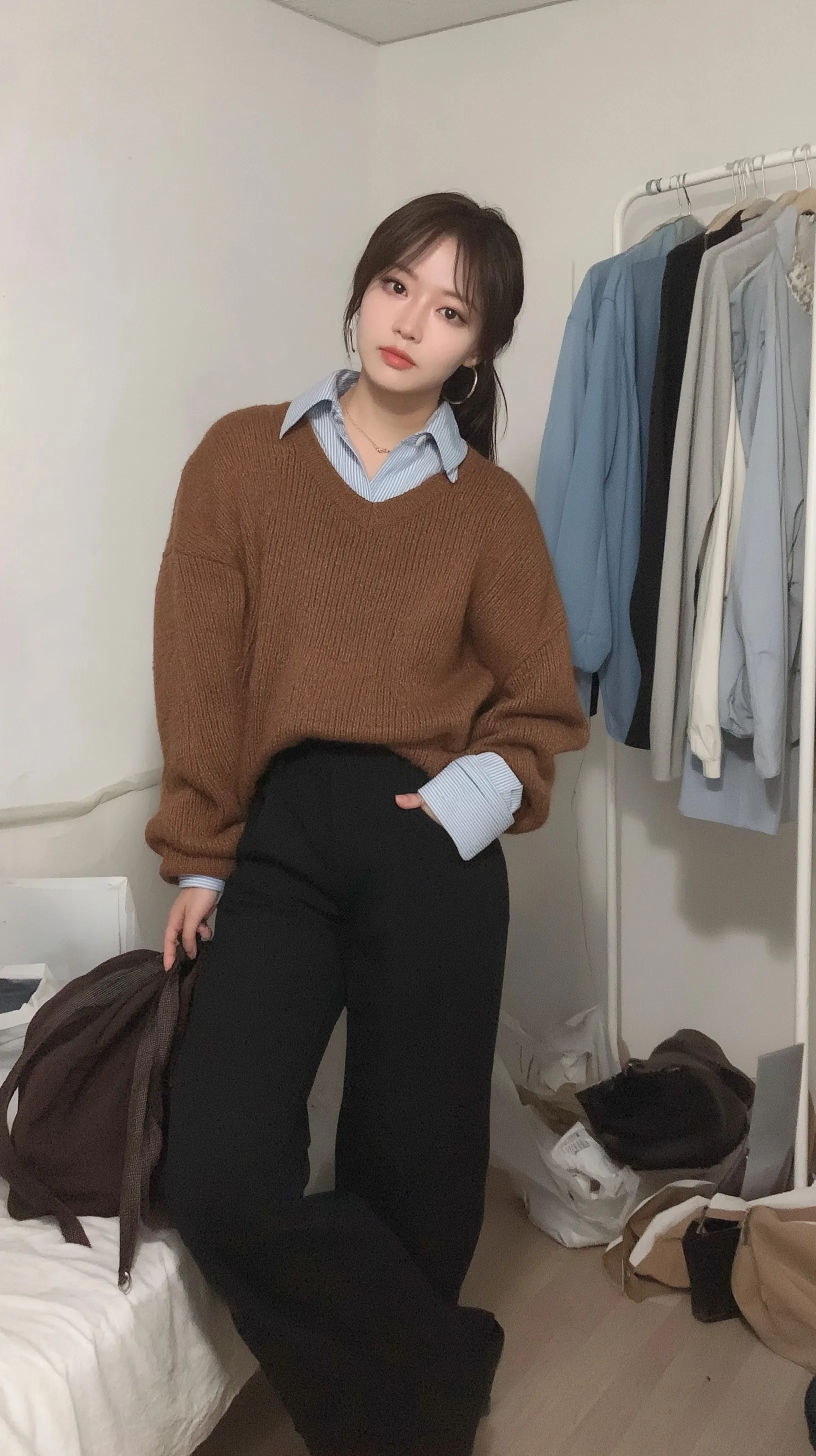 A Korean woman wearing an orange knit sweater, blue shirt, and black wide-leg pants for a first date outfit.