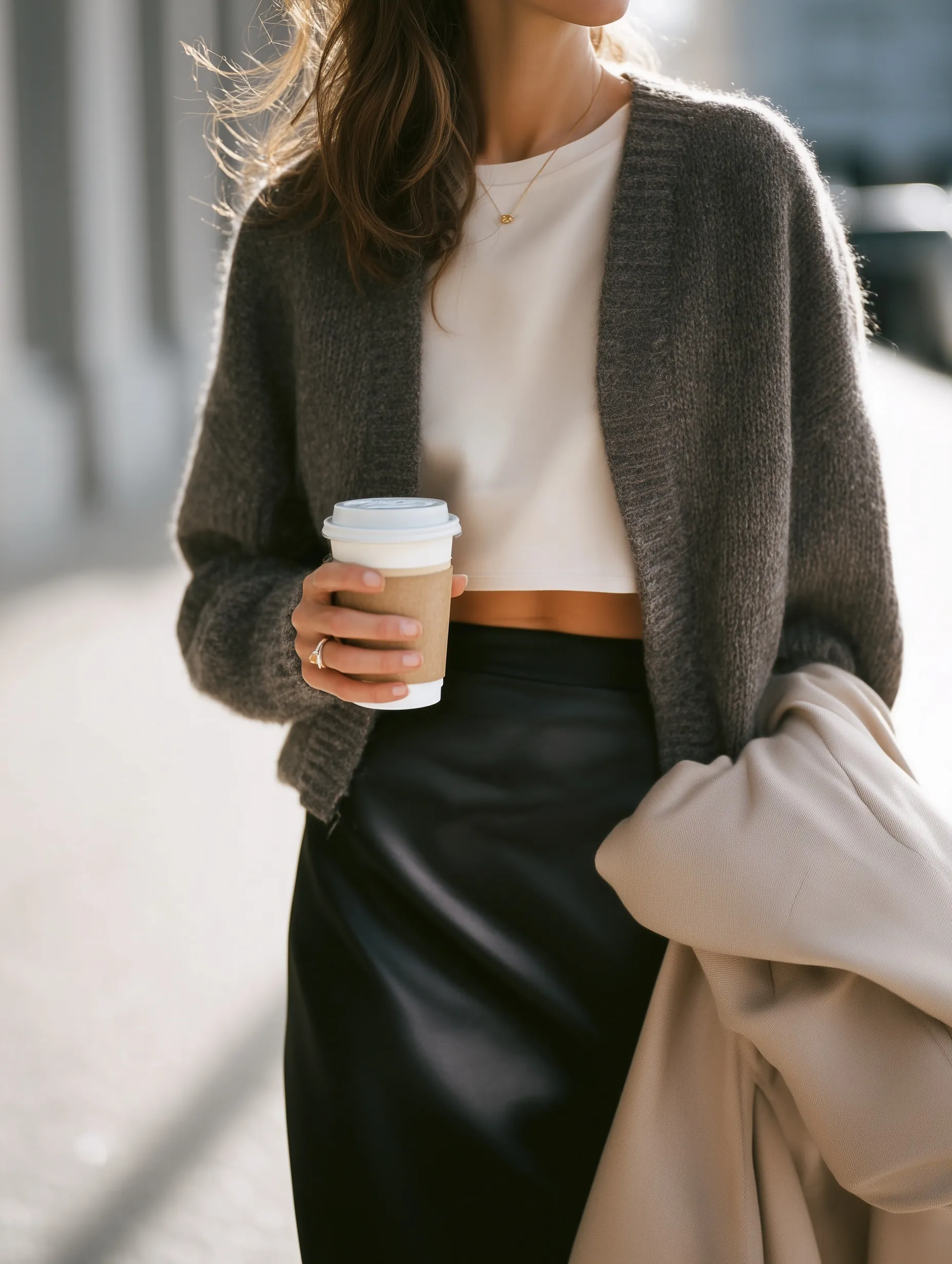 A woman in a charcoal cardigan and satin skirt holding a coffee cup, street style fashion for a first date.