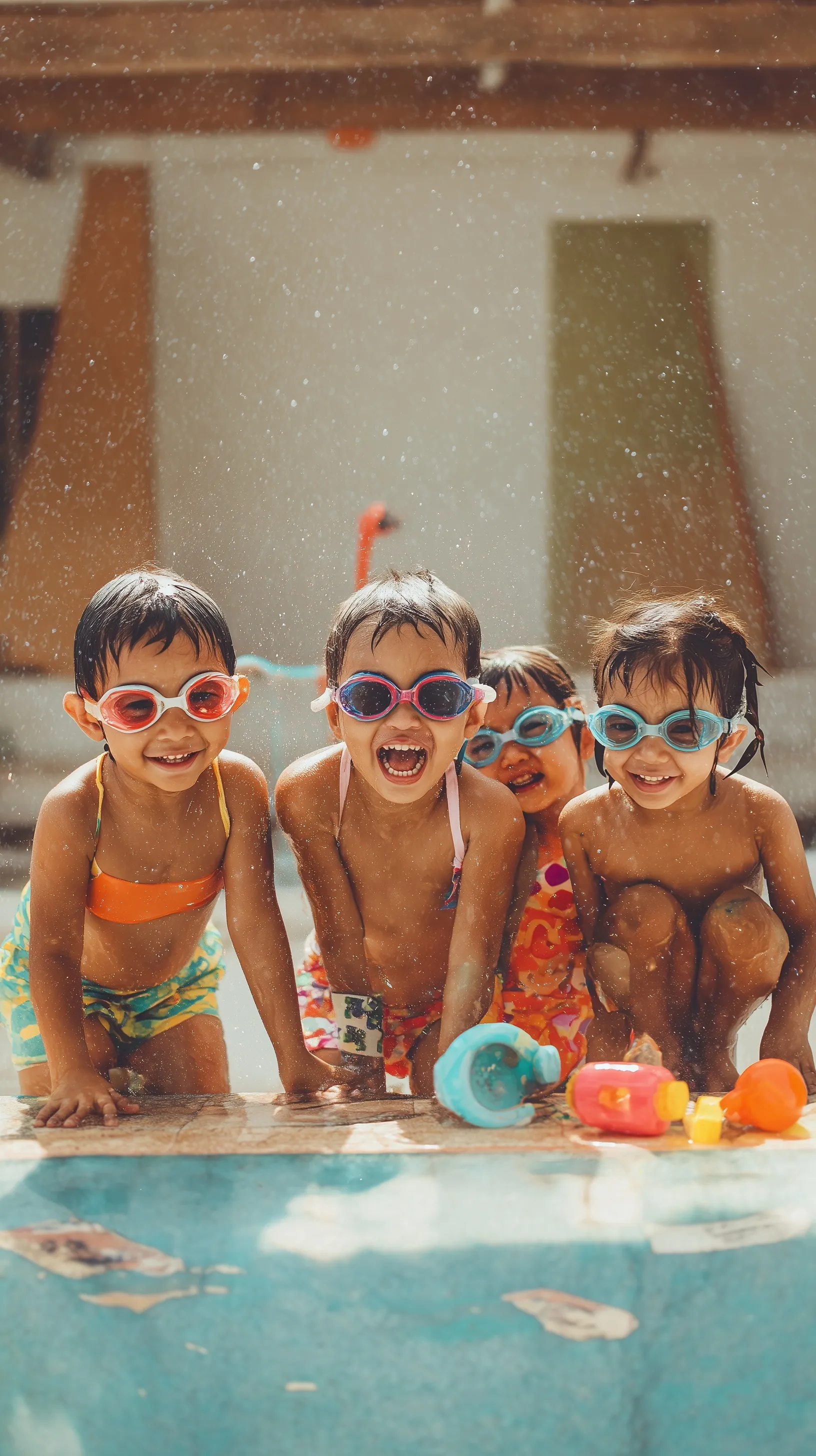 Joyful Mexican children wearing swimming goggles and splashing in an indoor pool during a fun summer party.