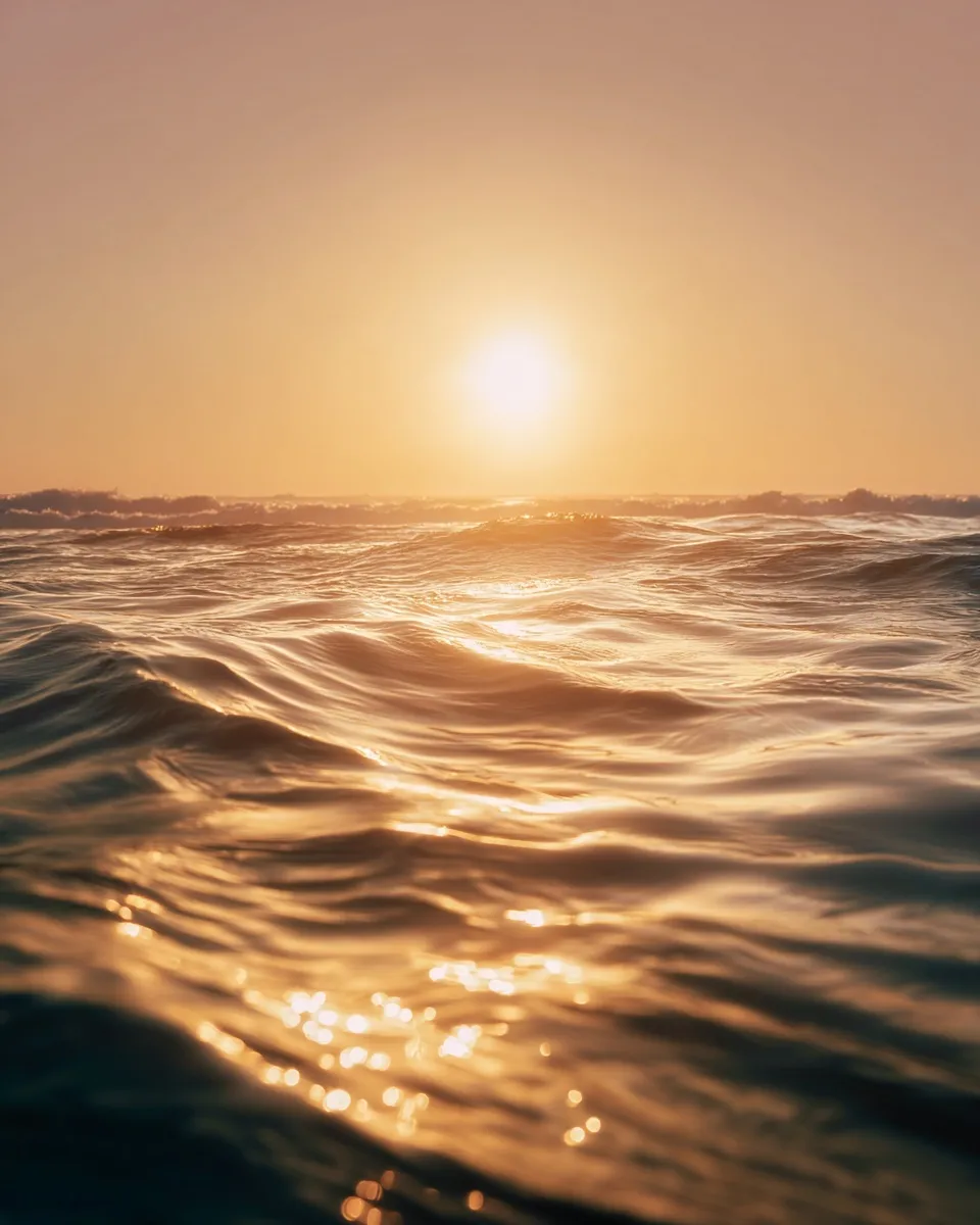 Golden hour at the ocean with gentle ripples, soft sunset light, and a minimalist horizon in a wide-angle view.