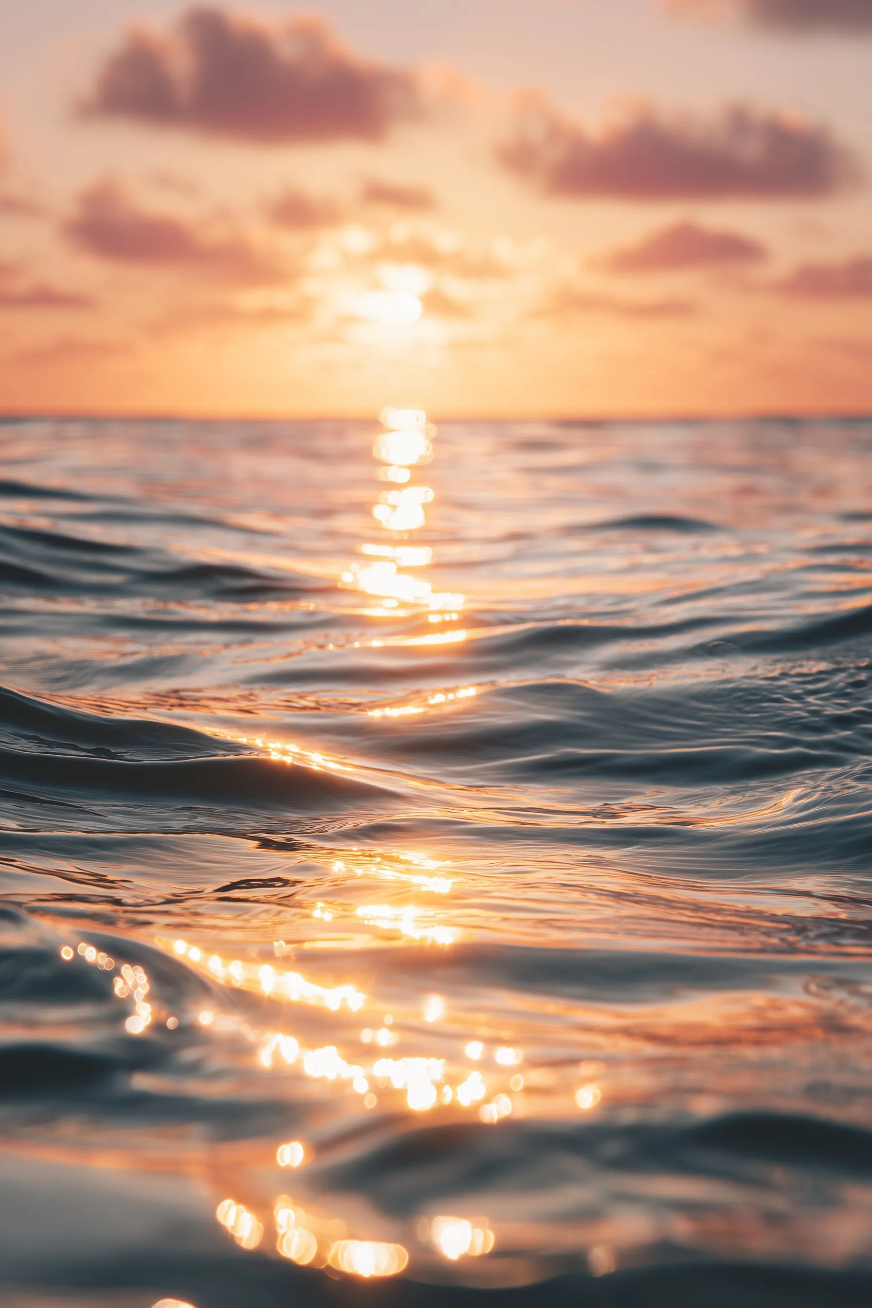 Close-up of calm ocean water with soft golden hour reflections, pink and orange sunset light, and dreamy ripples.