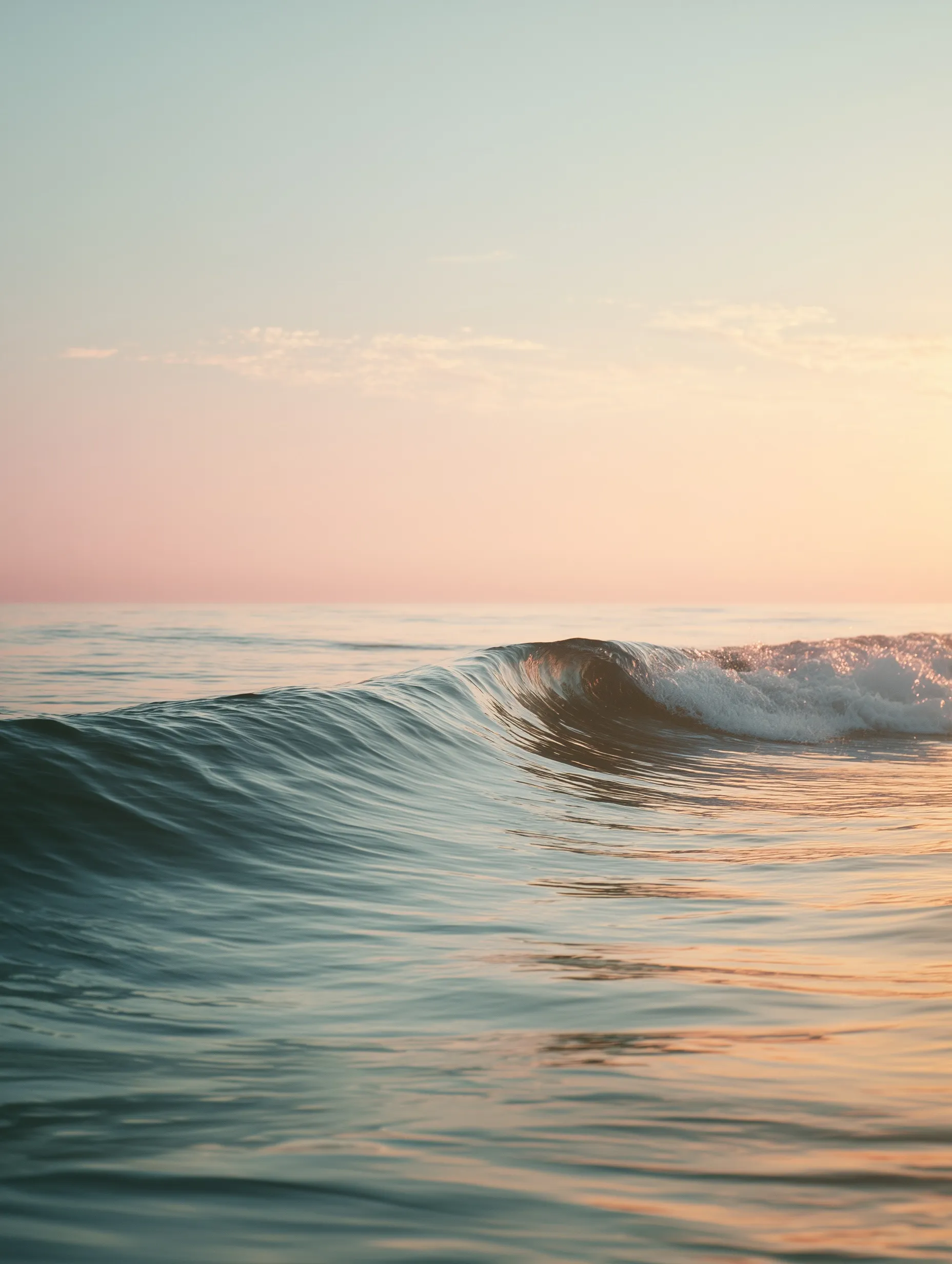 Minimalist fine art photo of a single ocean wave during a golden hour sunrise with soft peach and blue tones.