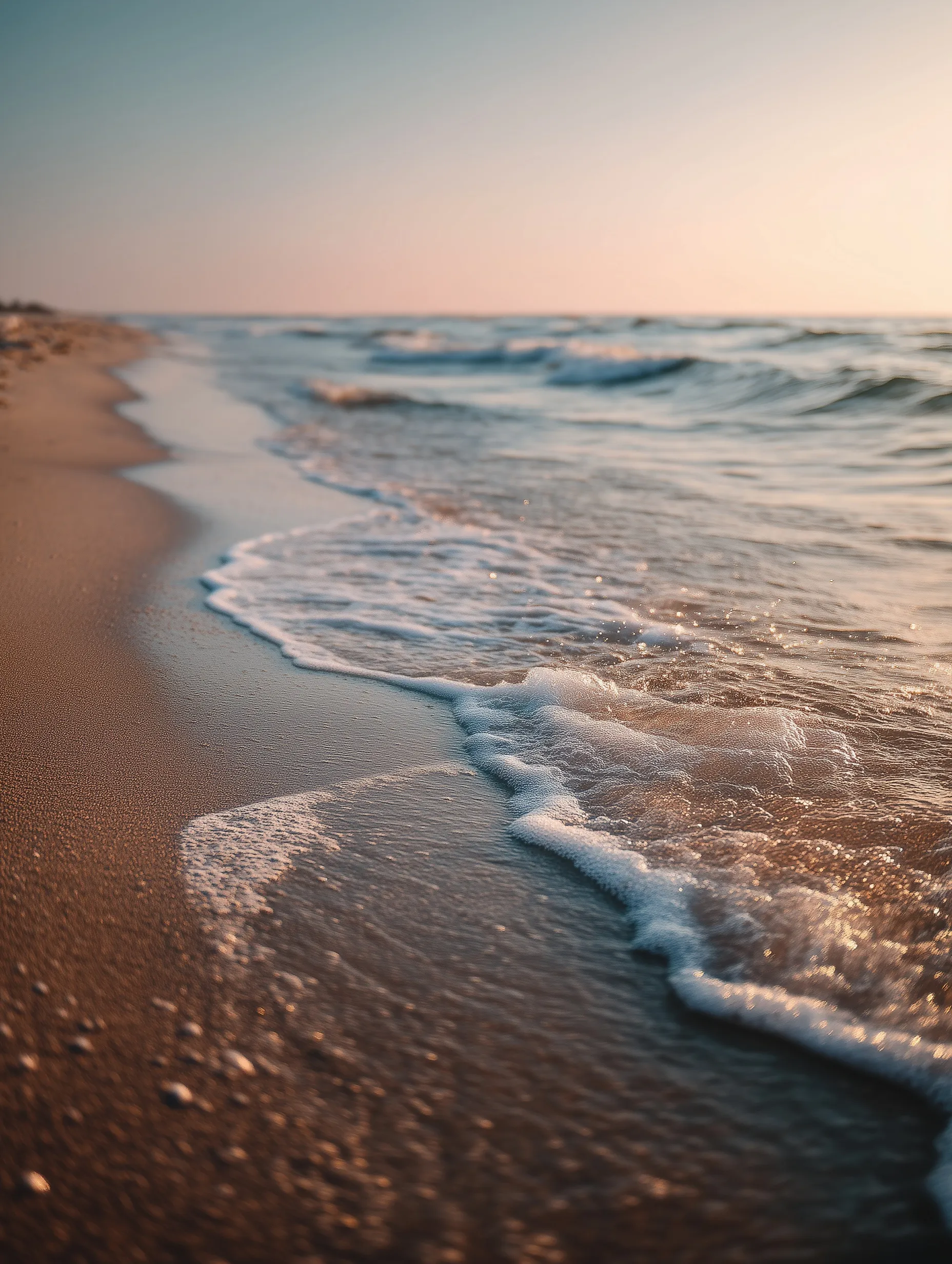 Empty beach at golden hour with wet sand, soft waves, and a peaceful pastel sky, cinematic low-angle view.