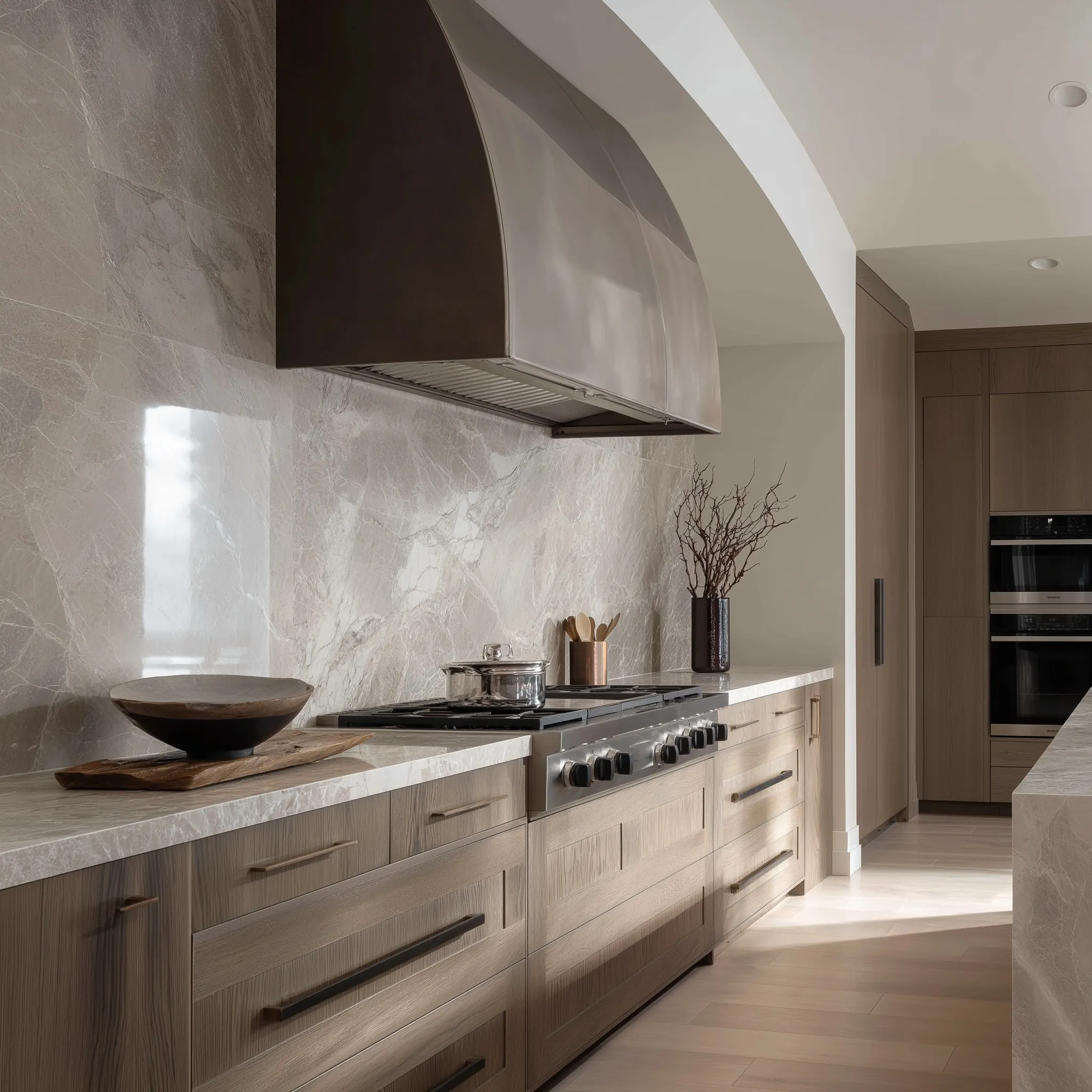 Ultra-luxury Italian kitchen with custom silver curved vent hood, oak cabinetry, and marble flooring.