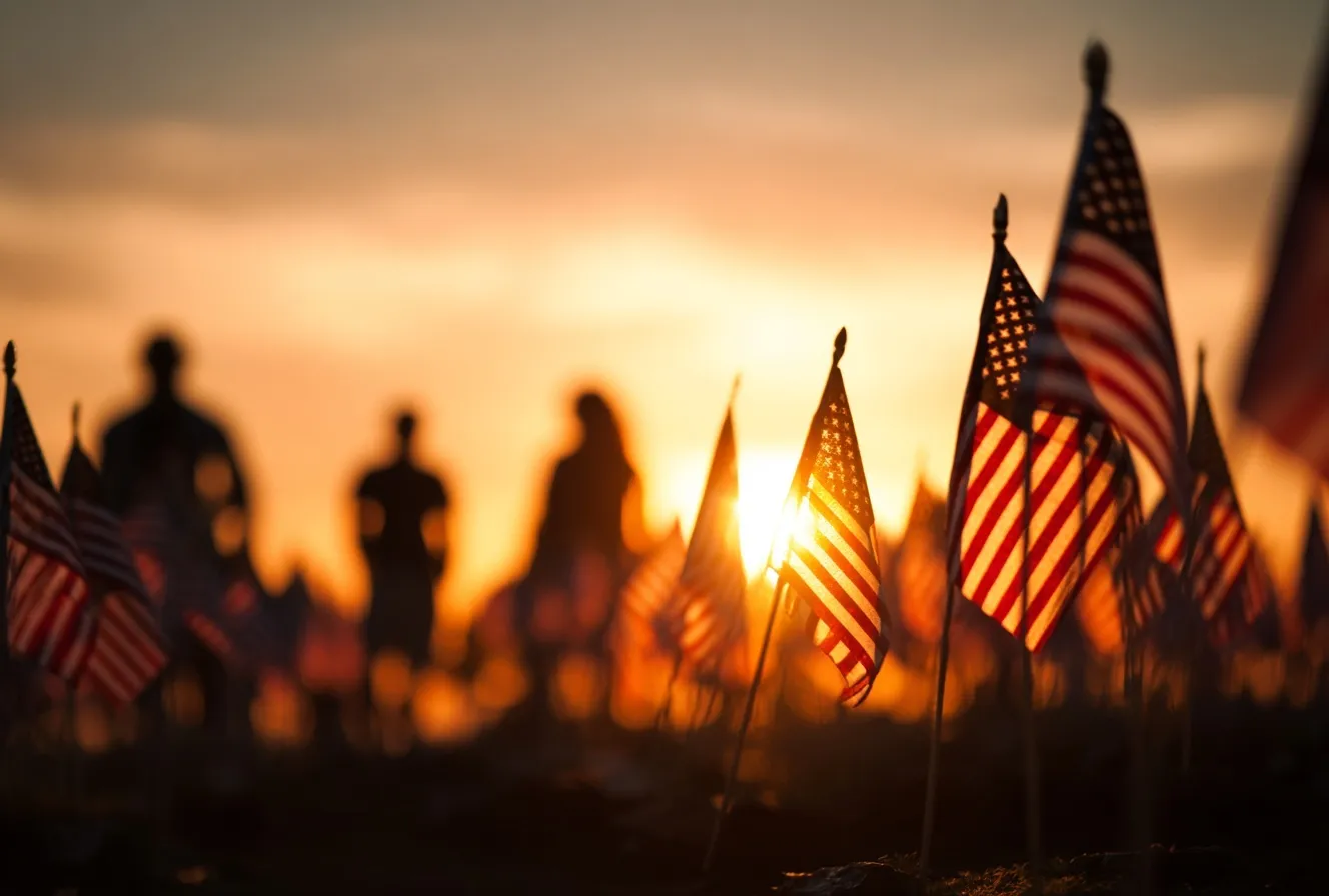 Visitors paying respects at a national cemetery filled with American flags during a vibrant Memorial Day sunset.