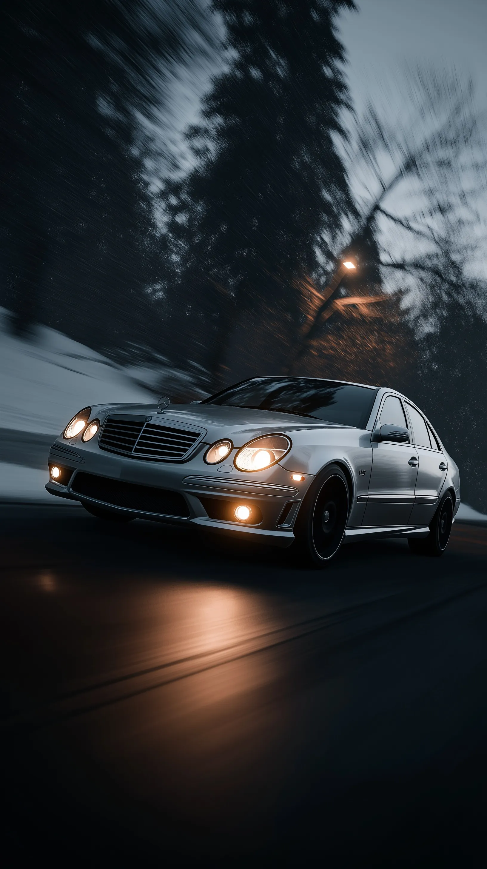 Mercedes W211 E550 in Iridium Silver drifting on a wintry night road with motion blur and amber fog lights.