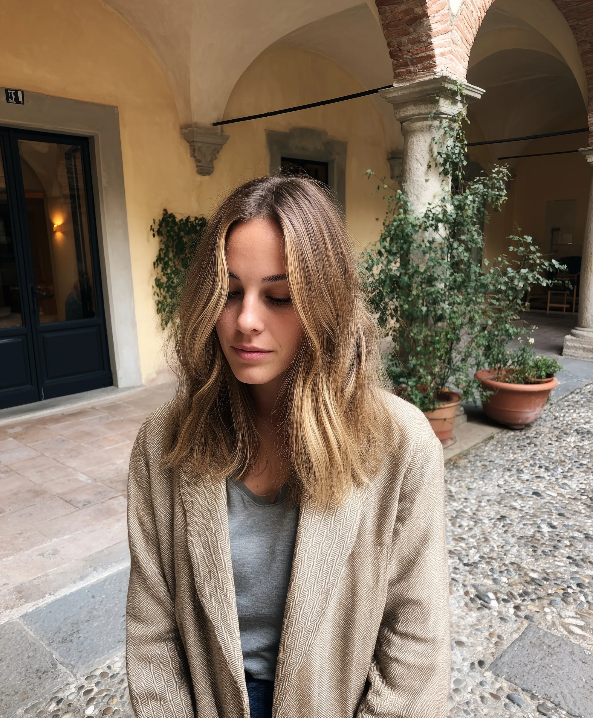 Candid photo of a woman with honey blonde shoulder-length balayage hair in an Italian salon courtyard.