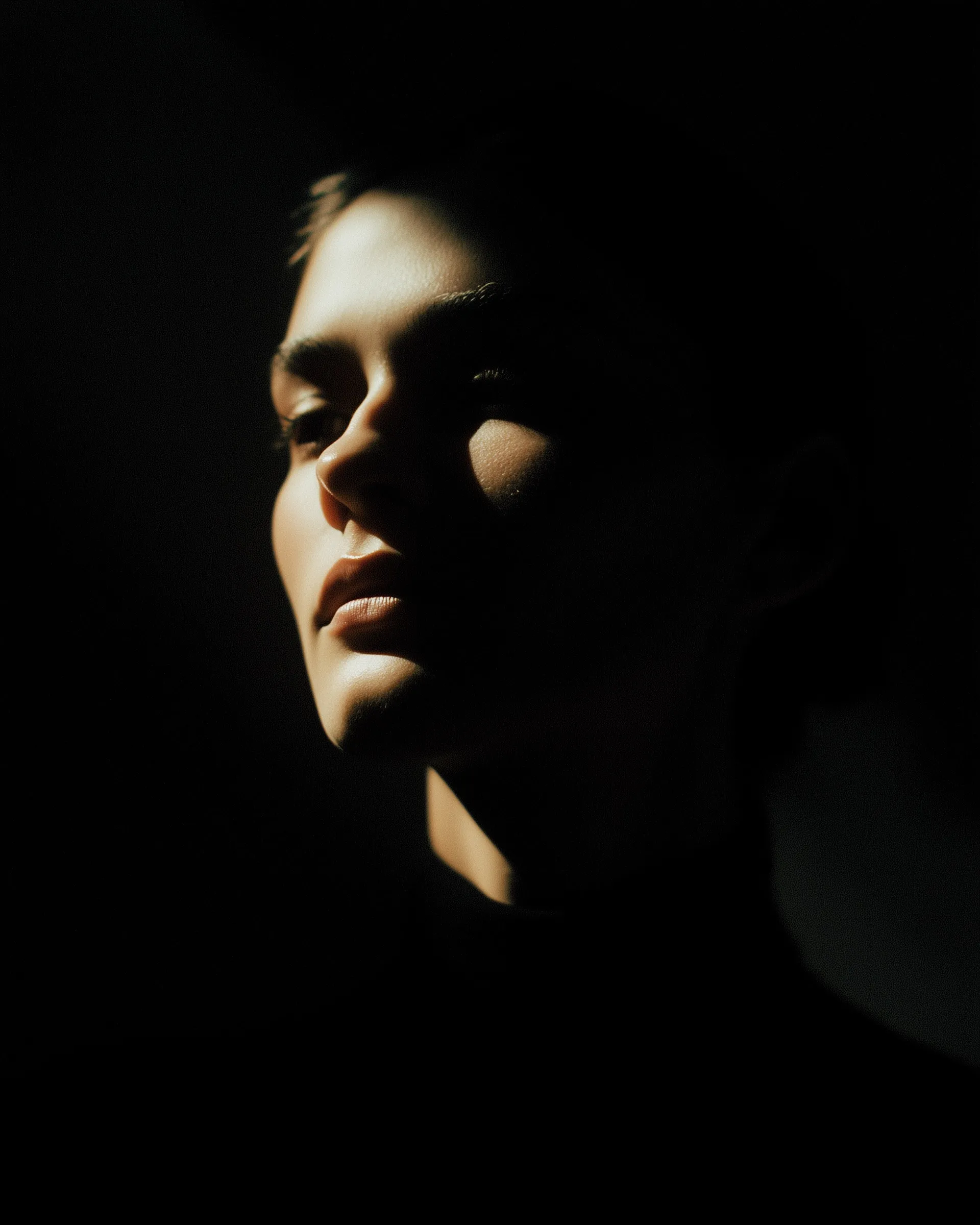 A cinematic close-up portrait of a fashion model using dramatic chiaroscuro lighting and high contrast shadows.