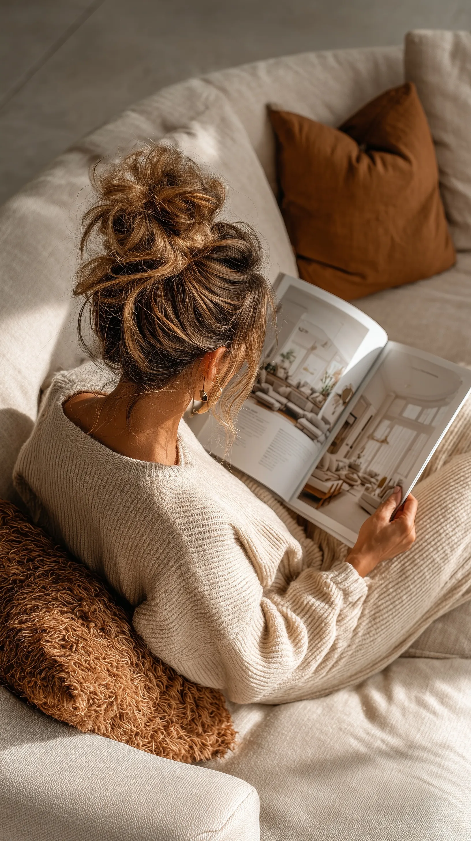 Woman in a cozy cream oversized lounge set reading an interior design magazine on a beige sofa.