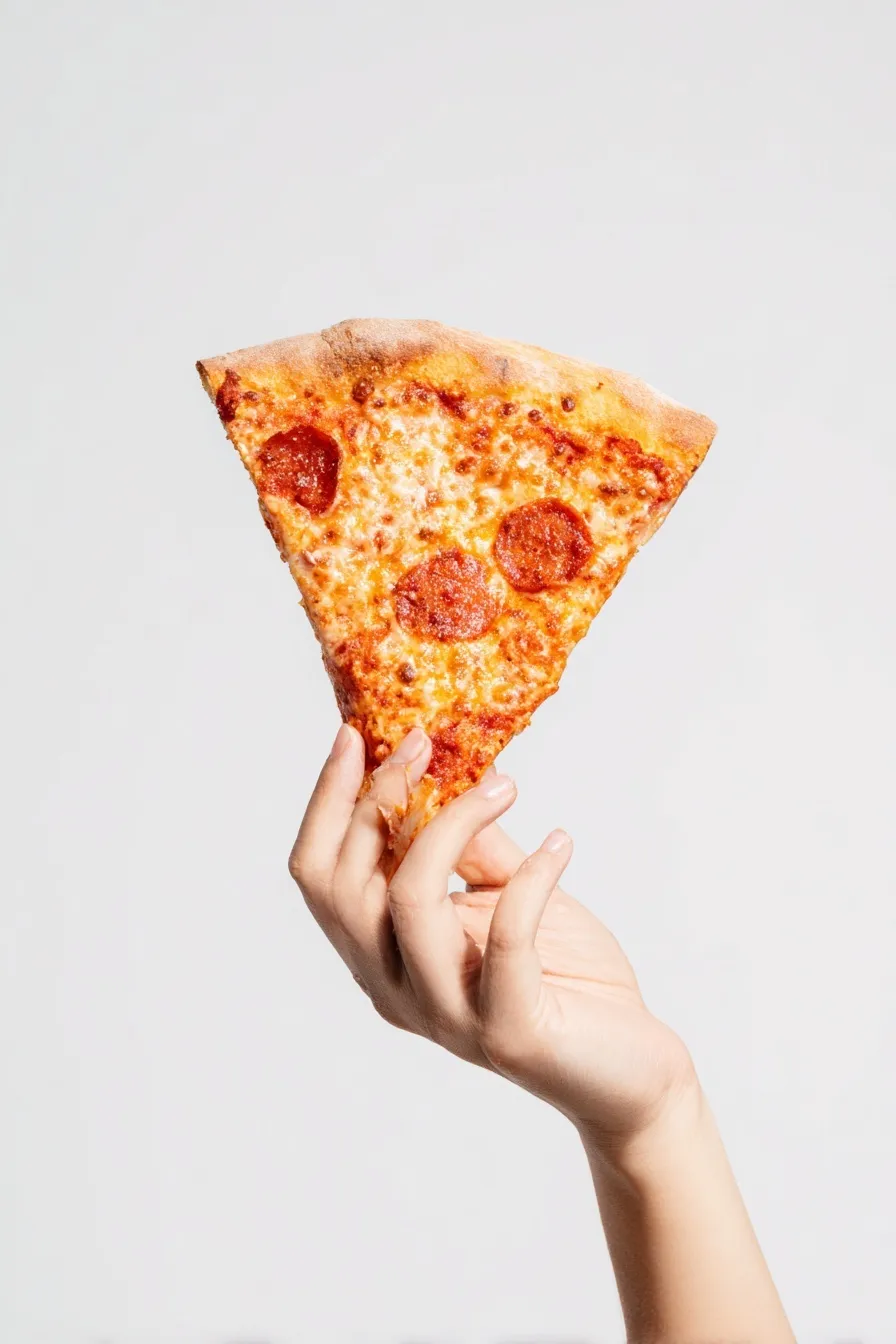 A hand holding a delicious pizza slice isolated on a clean white background, minimalist food photography.
