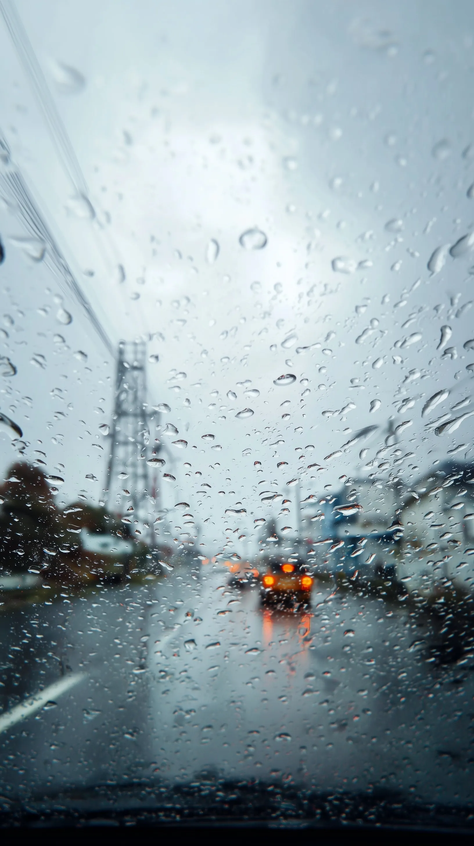 POV shot through a rain-covered car windshield looking out at a blurred suburban skyline and giant floating khinkali.
