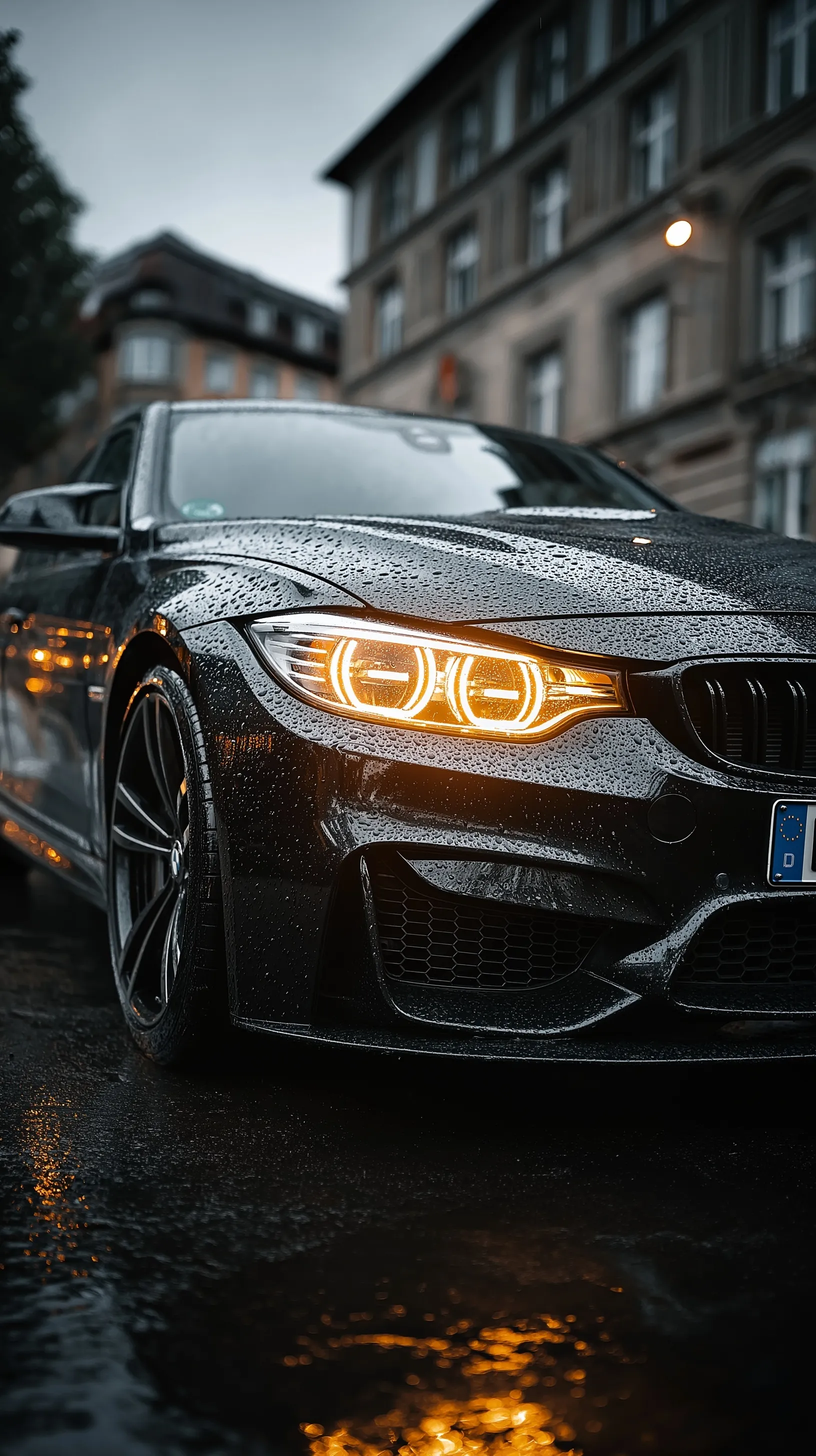 A cinematic low-angle shot of a BMW front bumper covered in rain droplets with dramatic reflections.