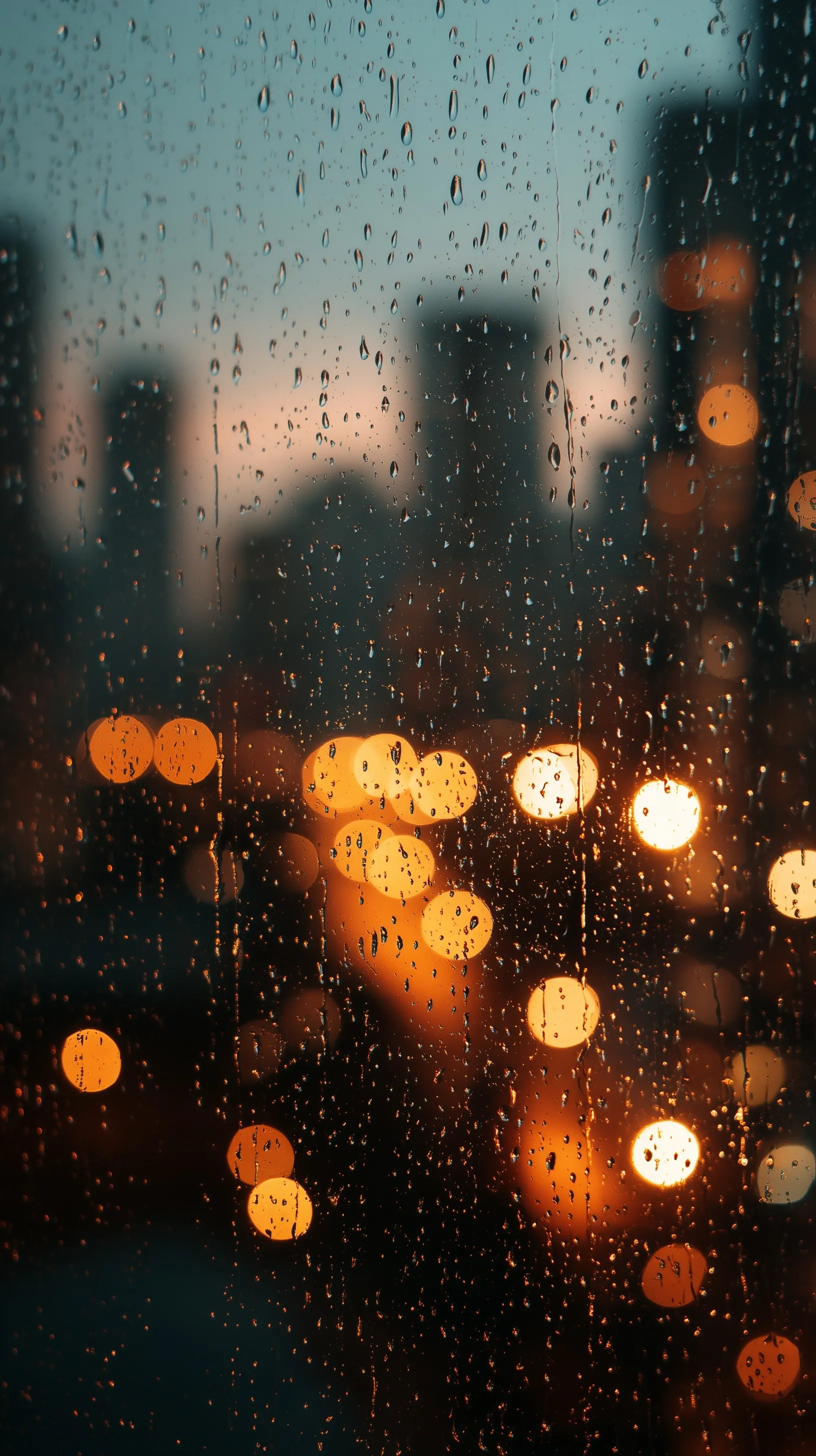 Raindrops on a windowpane with soft, blurry city lights creating a beautiful evening bokeh background.