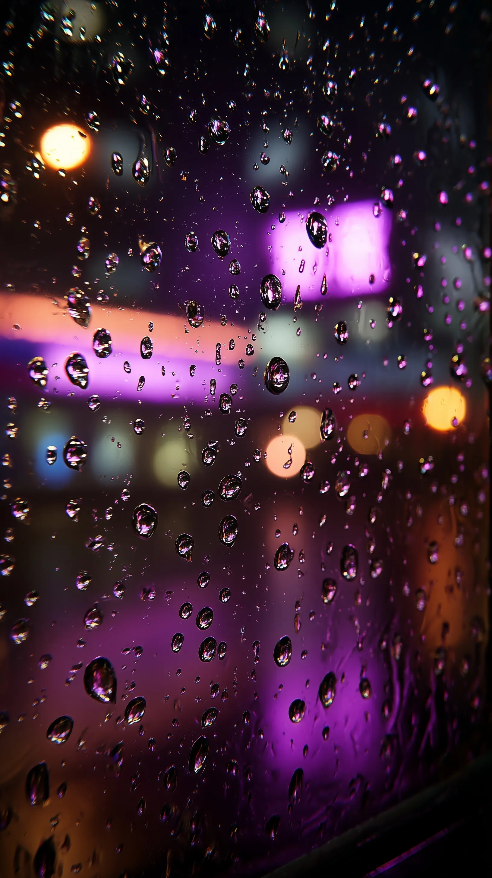 Macro close-up of neon purple raindrops on wet window glass with blurred city lights at night.