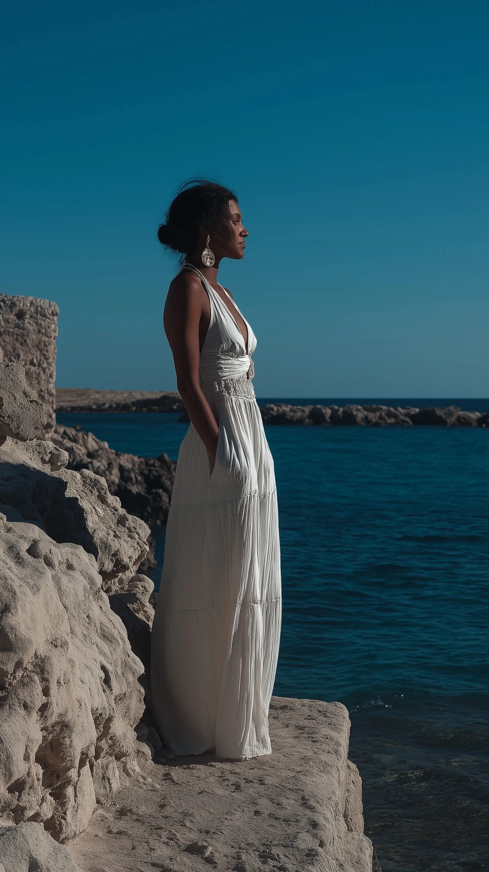 A woman wearing a long white summer dress standing by the sea in Santorini.