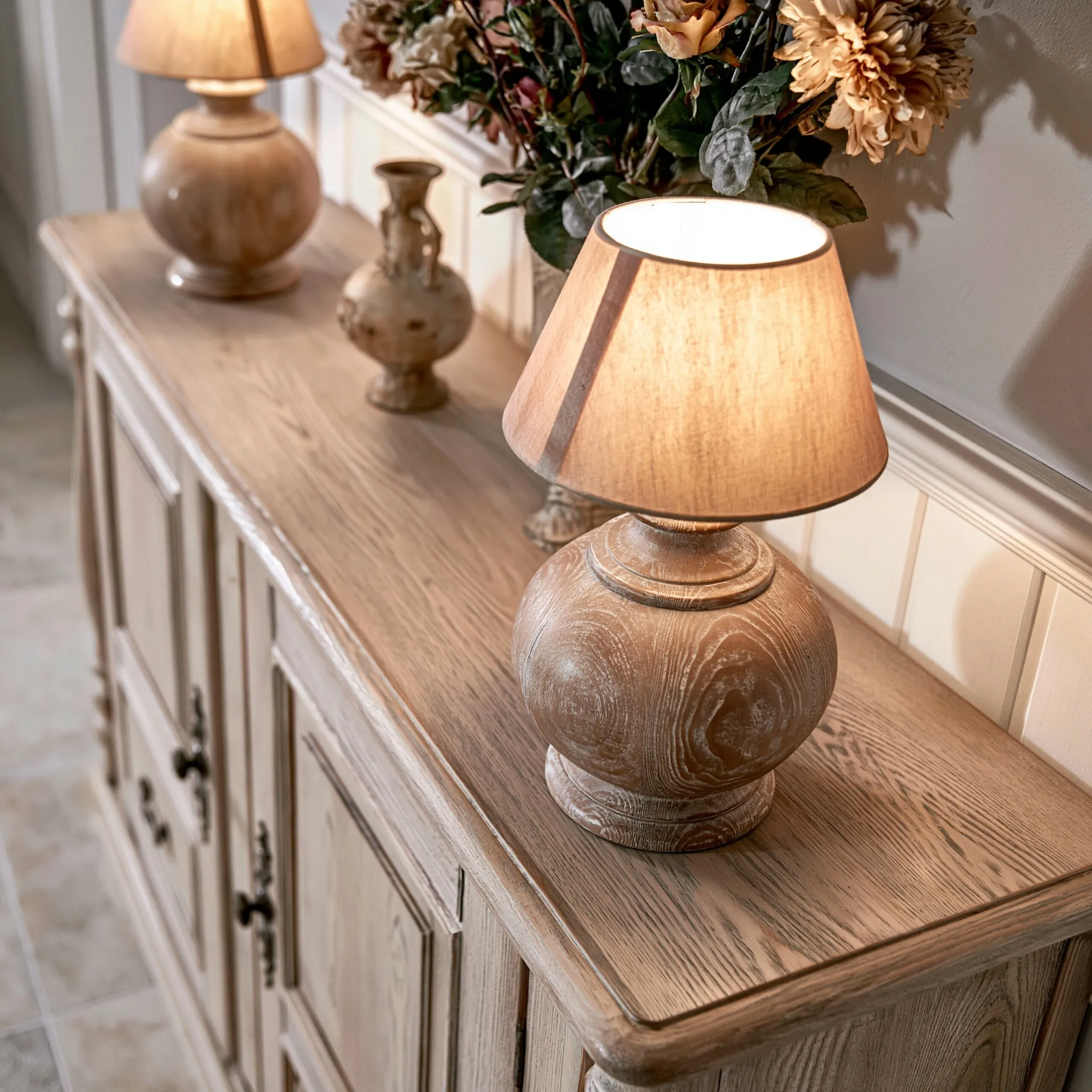 Antique wooden console table in an American-style living room with distressed lamps and floral decor.