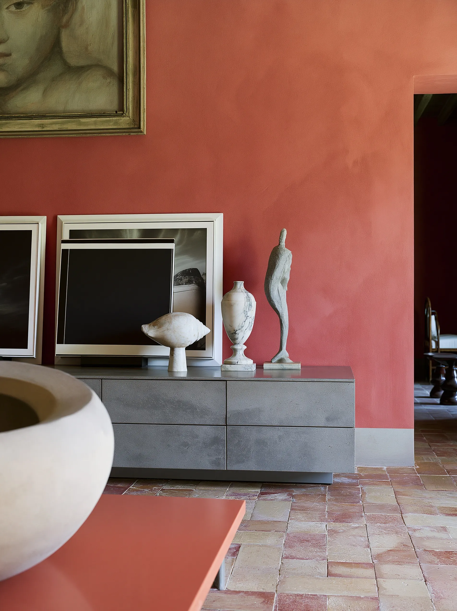 A modern small console table against a vibrant pink limewashed wall with contemporary art and marble sculptures.