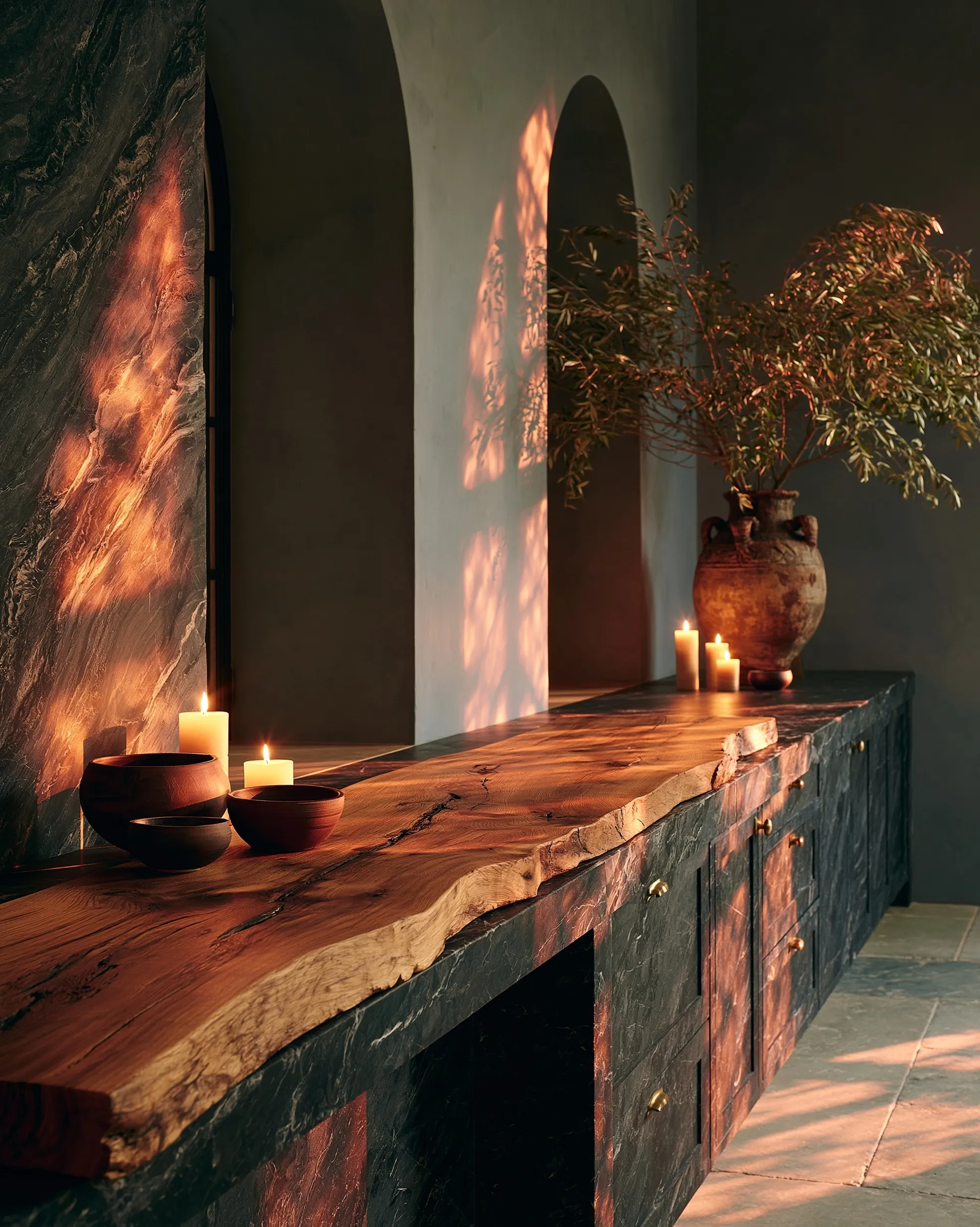A reclaimed oak console table in a moody, rustic kitchen with dark stone counters, pottery, and brass accents.