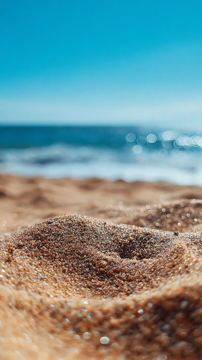 Close-up of golden beach sand with a blue ocean and sky background, bokeh effect, bright summer day.