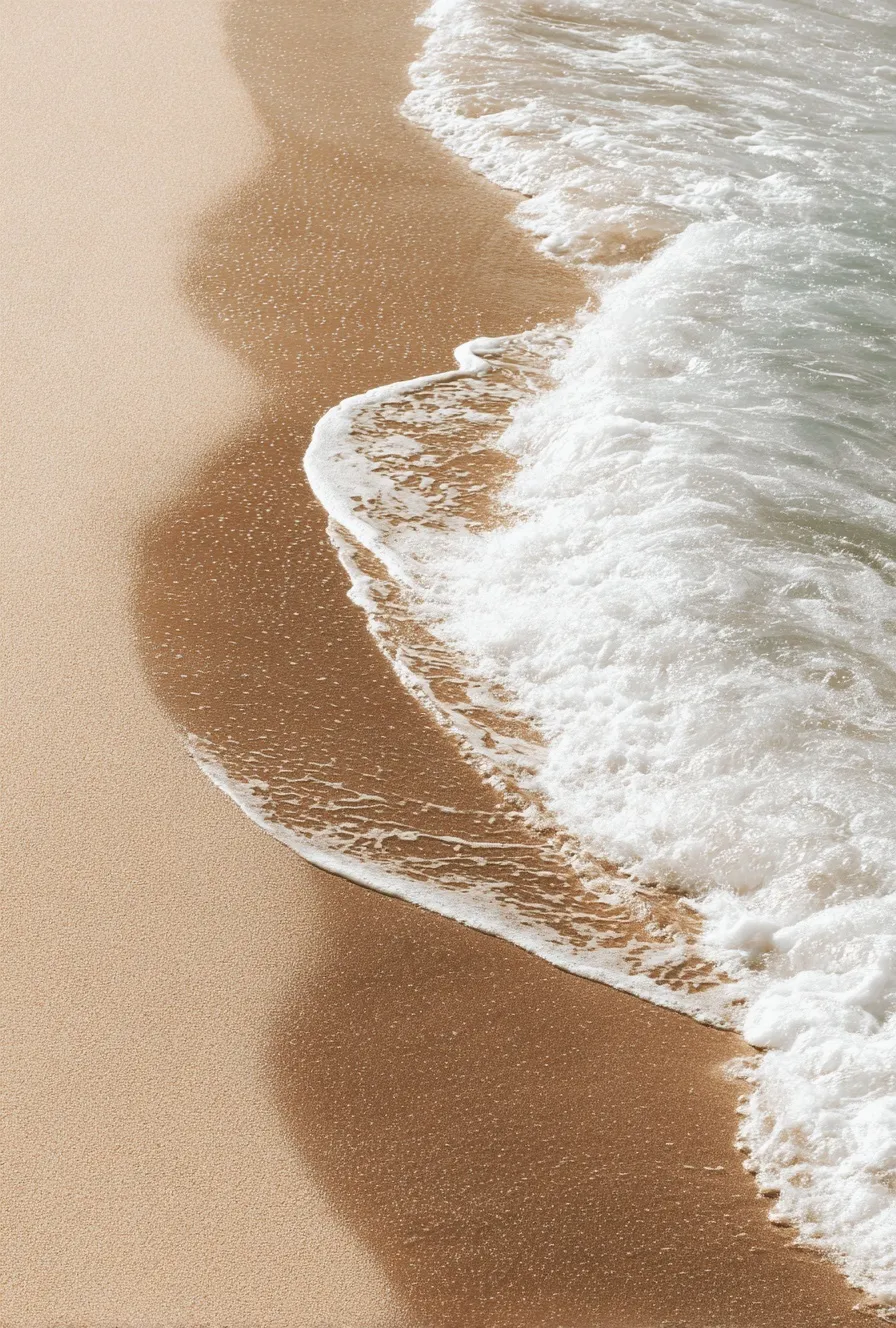 Aesthetic close-up of beige beach sand and white ocean waves under a bright summer sky in muted neutral tones.
