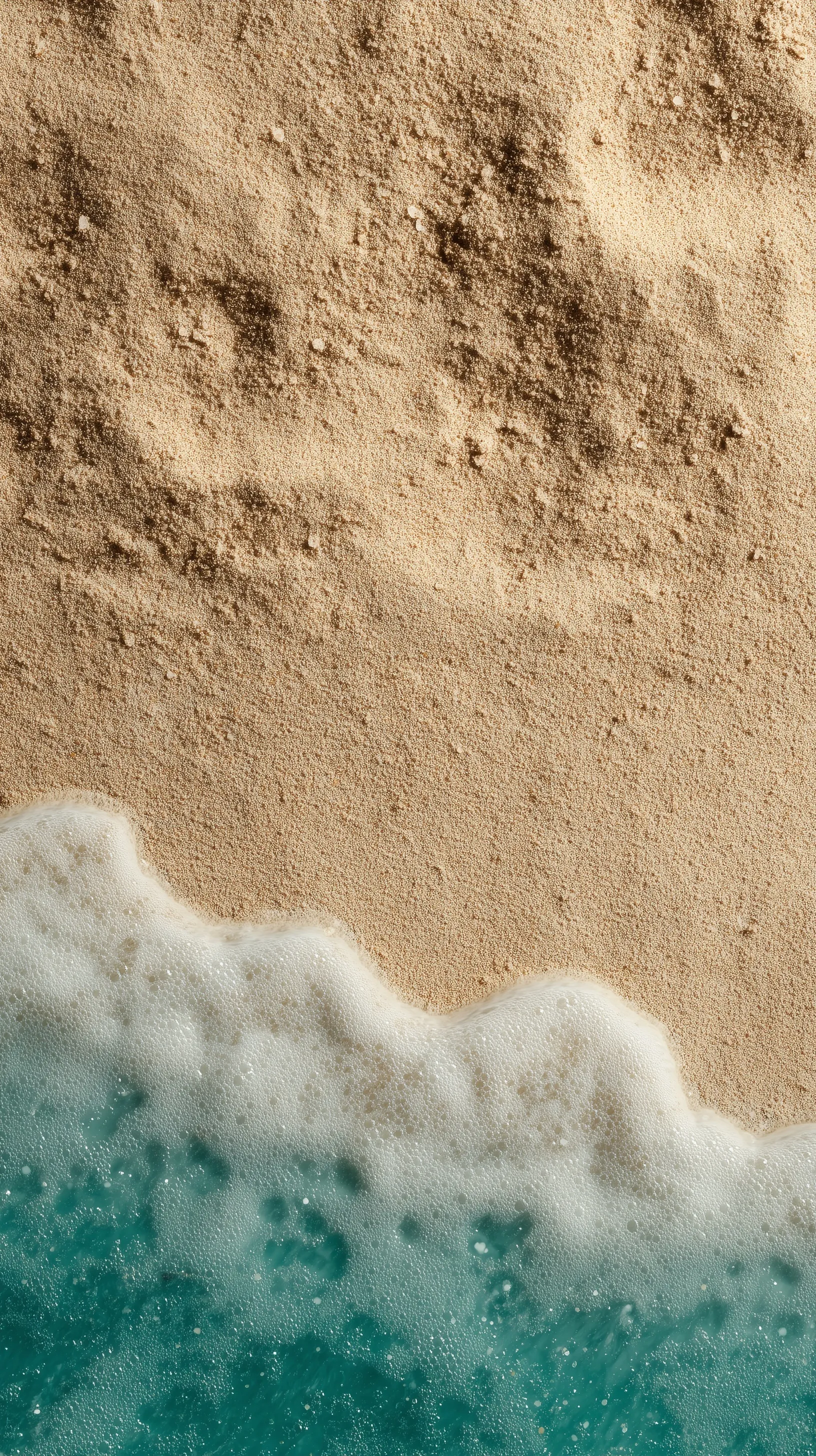Top-down view of beige sand texture meeting turquoise ocean water on a bright summer beach.