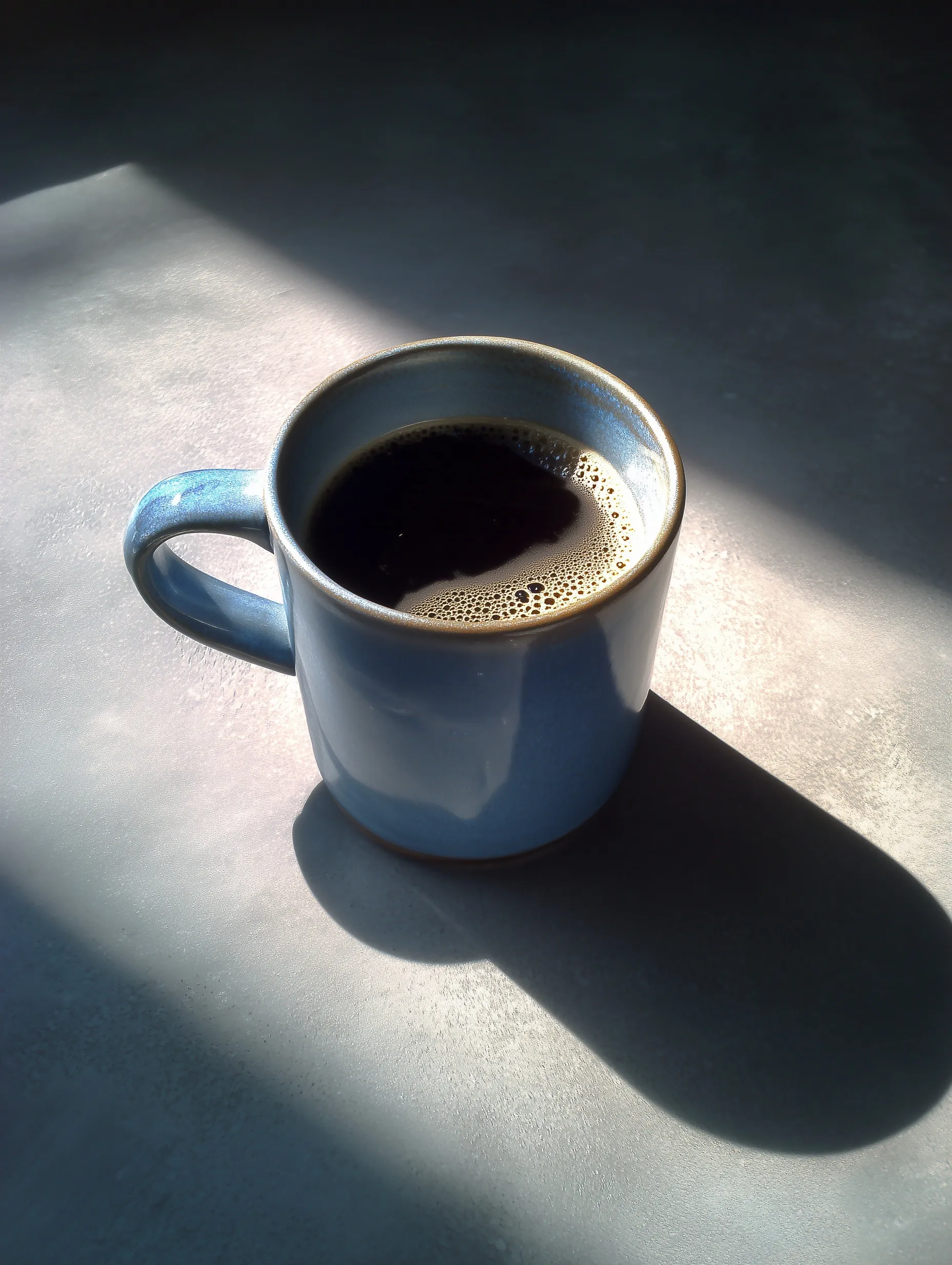 A retro, low-resolution photo of a handleless ceramic coffee mug on a smooth surface with natural sunlight.