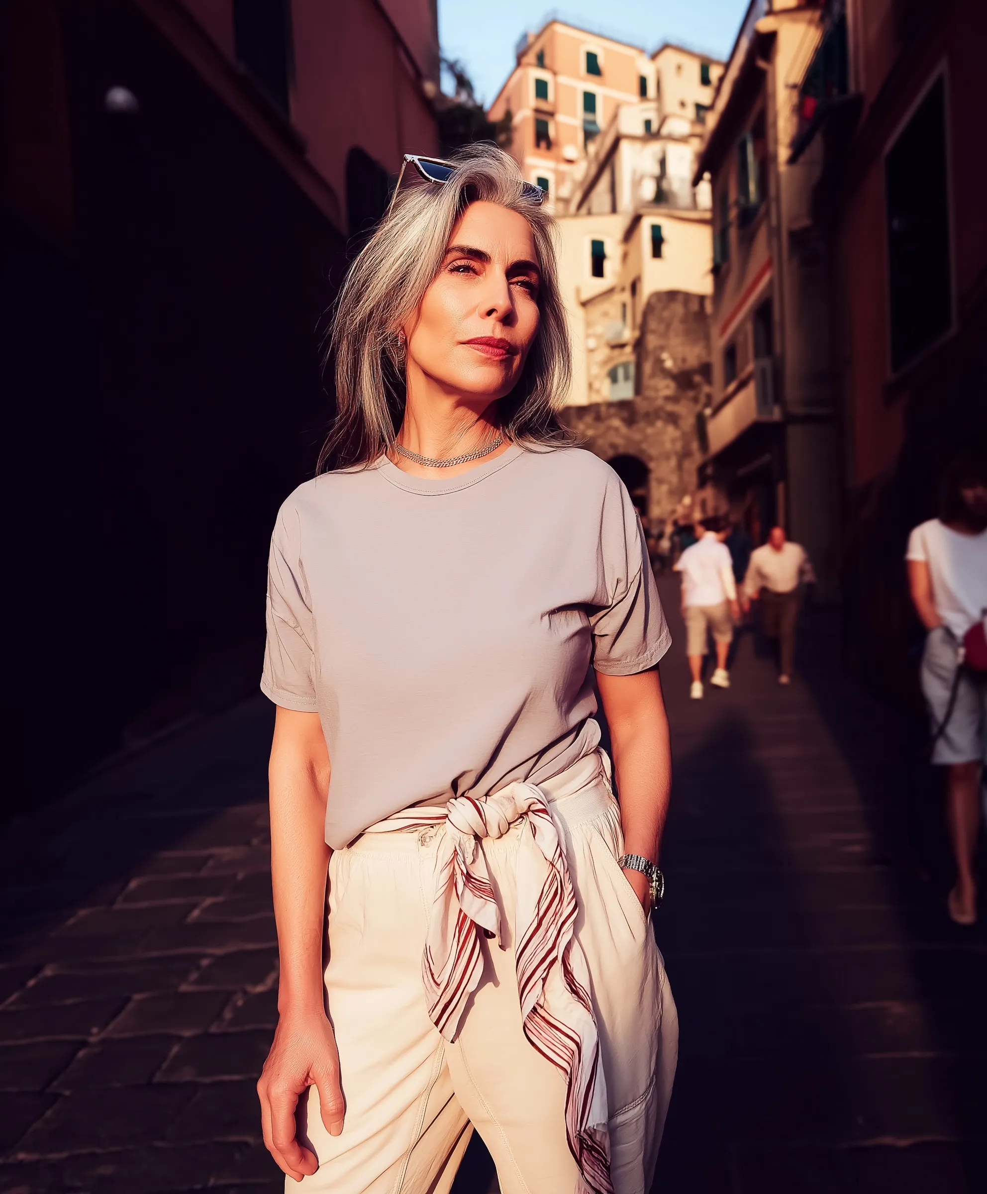 Stylish woman in 50s wearing a blank t-shirt and linen pants on a sunny European cobblestone street.