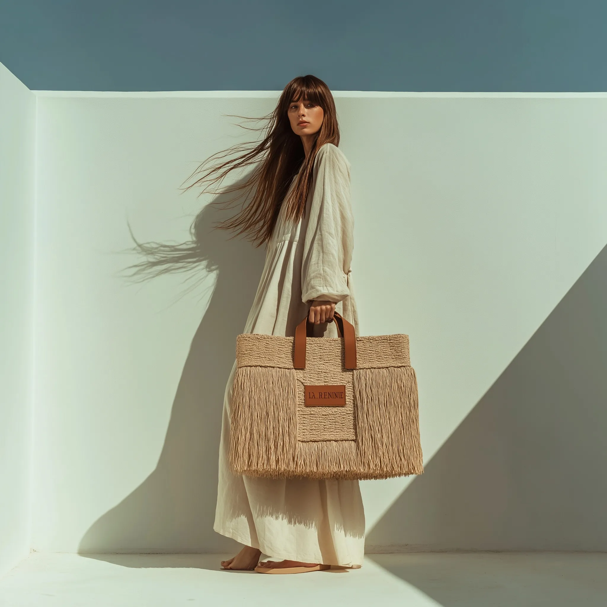 Elegant woman in a pastel dress posing with a stylish raffia fringe straw bag against a minimalist white background.